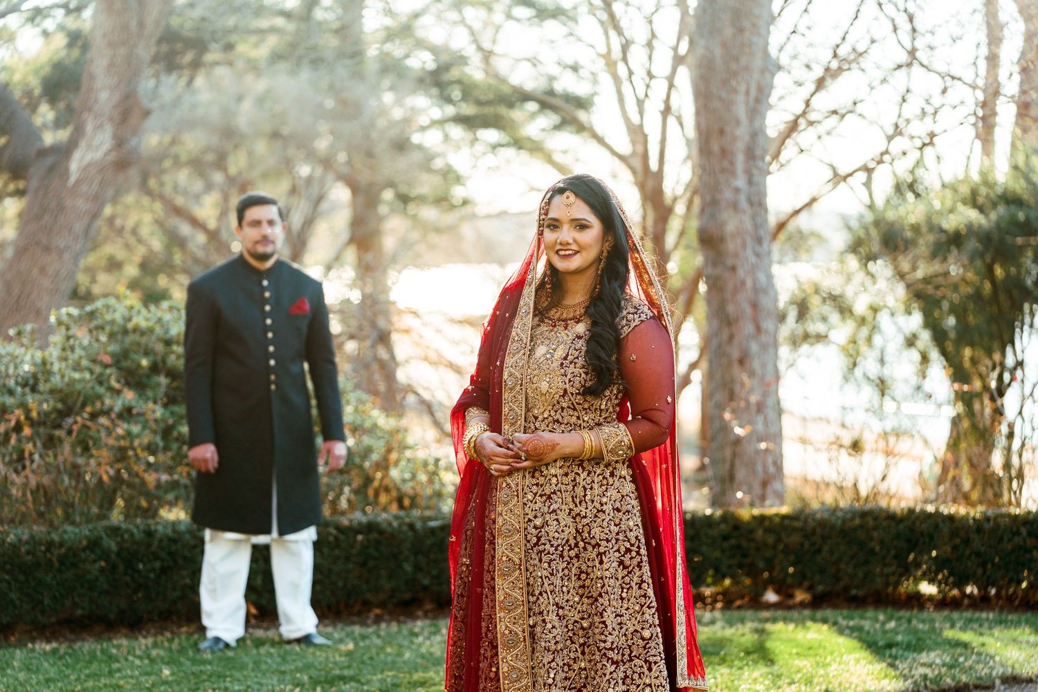 Wedding couple takes romantic portraits in outdoor garden setting wearing traditional South Asian attire.
