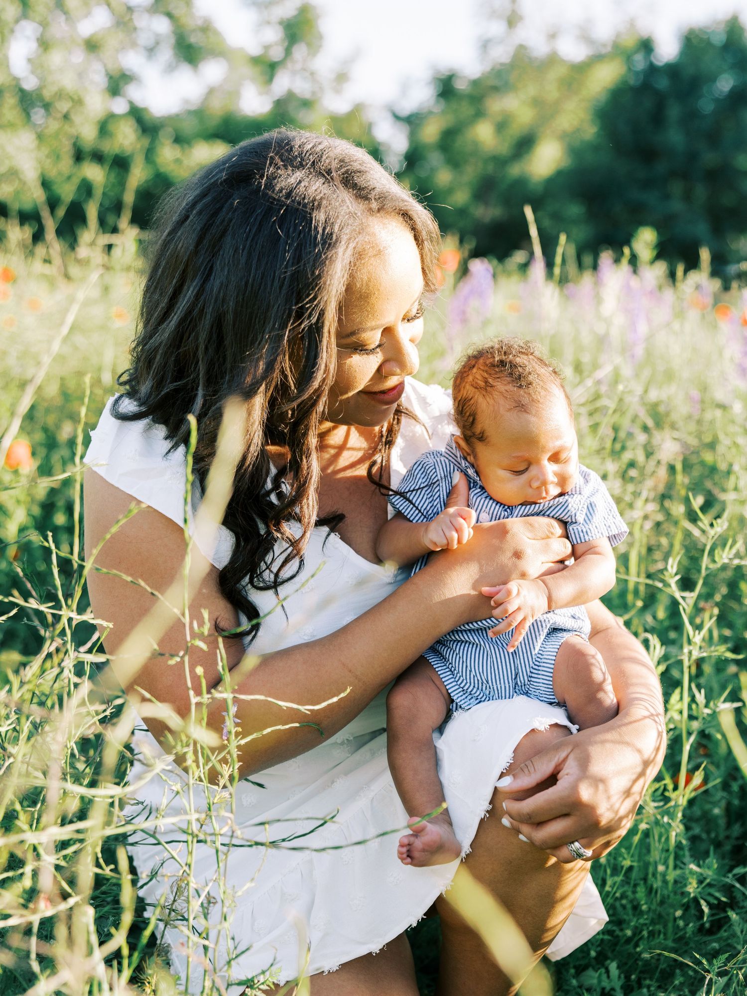 A tender moment captured in a wildflower meadow on a sunny summer day as a baby is held and kissed.