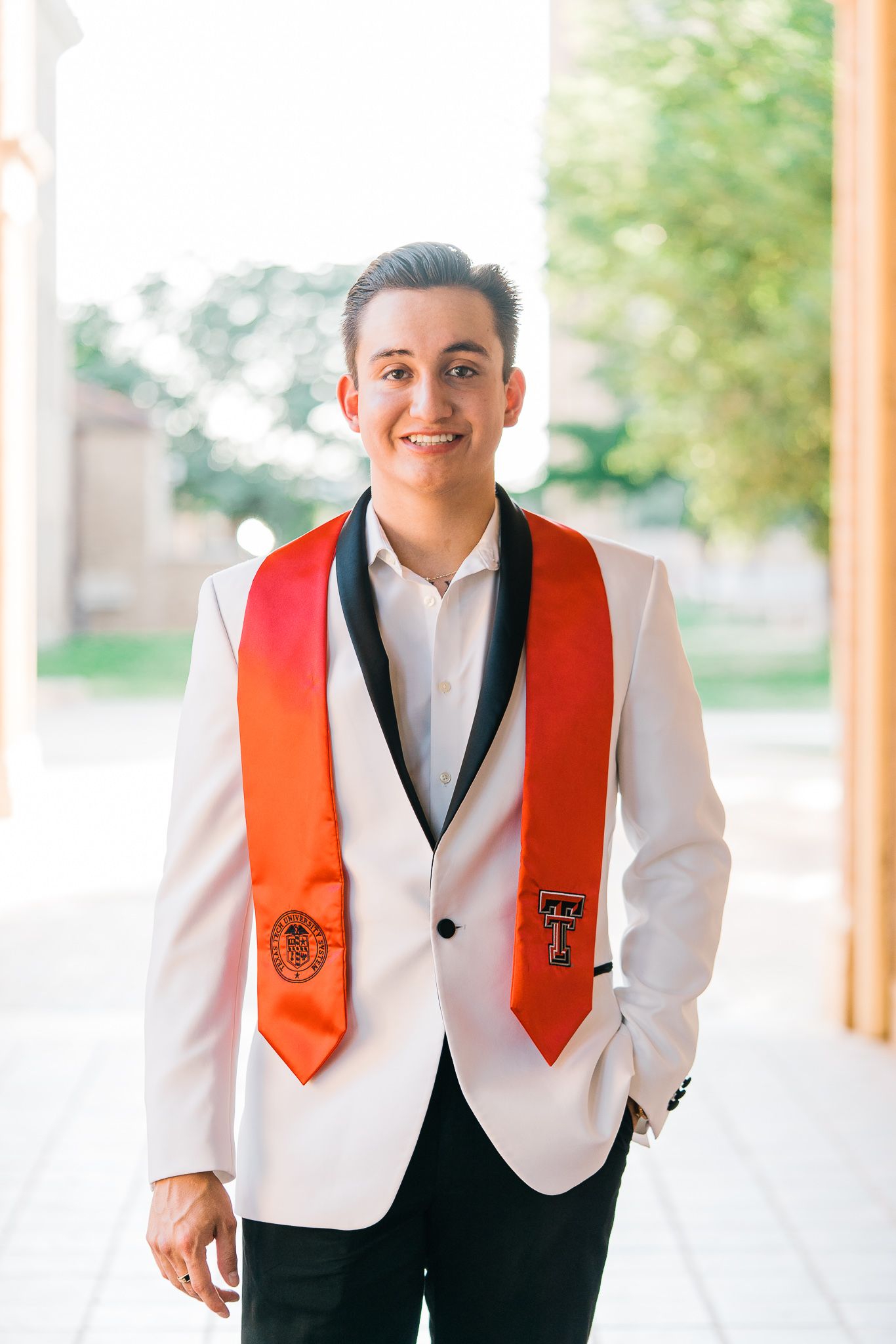 Graduate in white dress shirt and orange stole smiles brightly in outdoor portrait session.