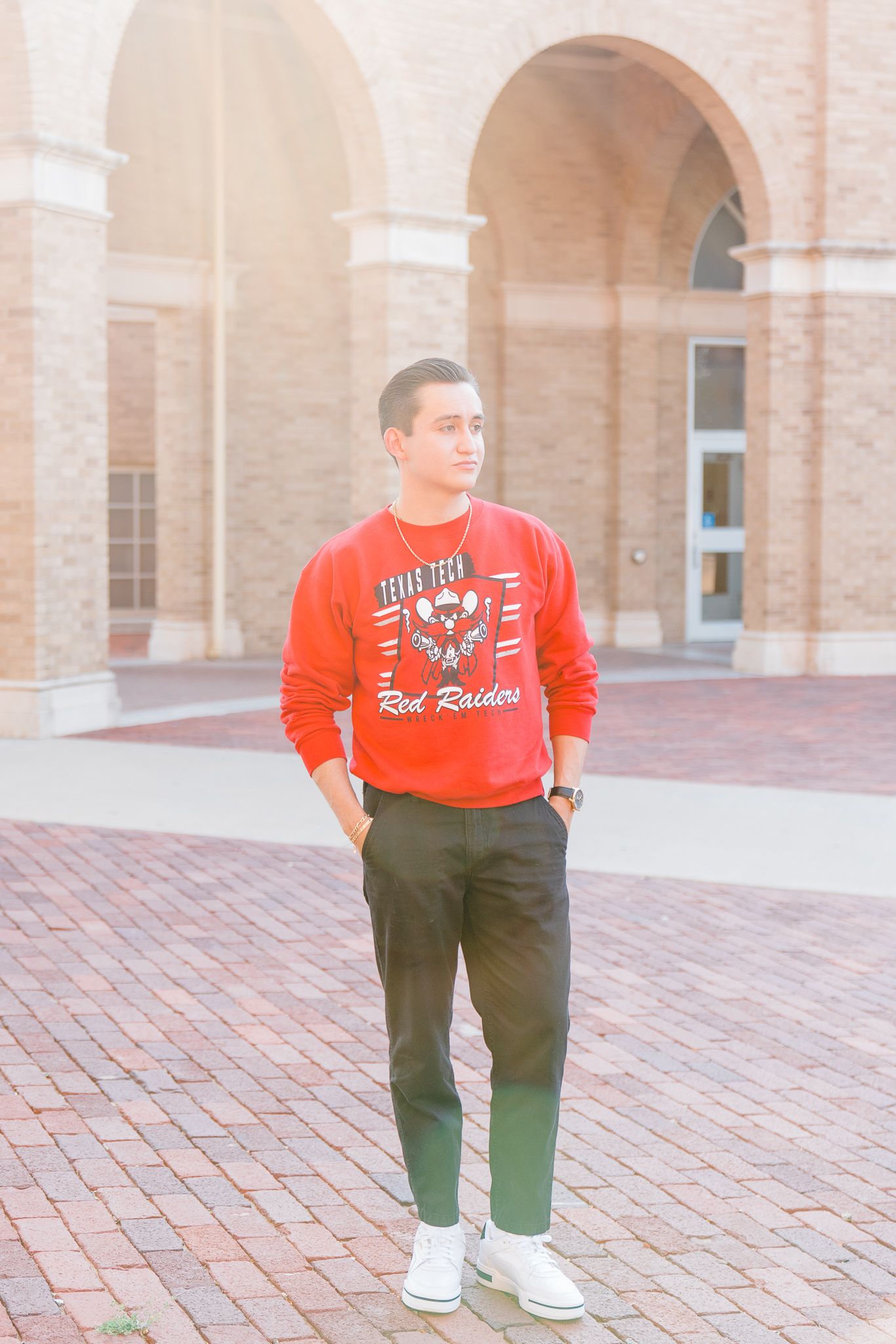 Person wearing a bright red sweatshirt and dark pants stands on brick pavement near a brick building.