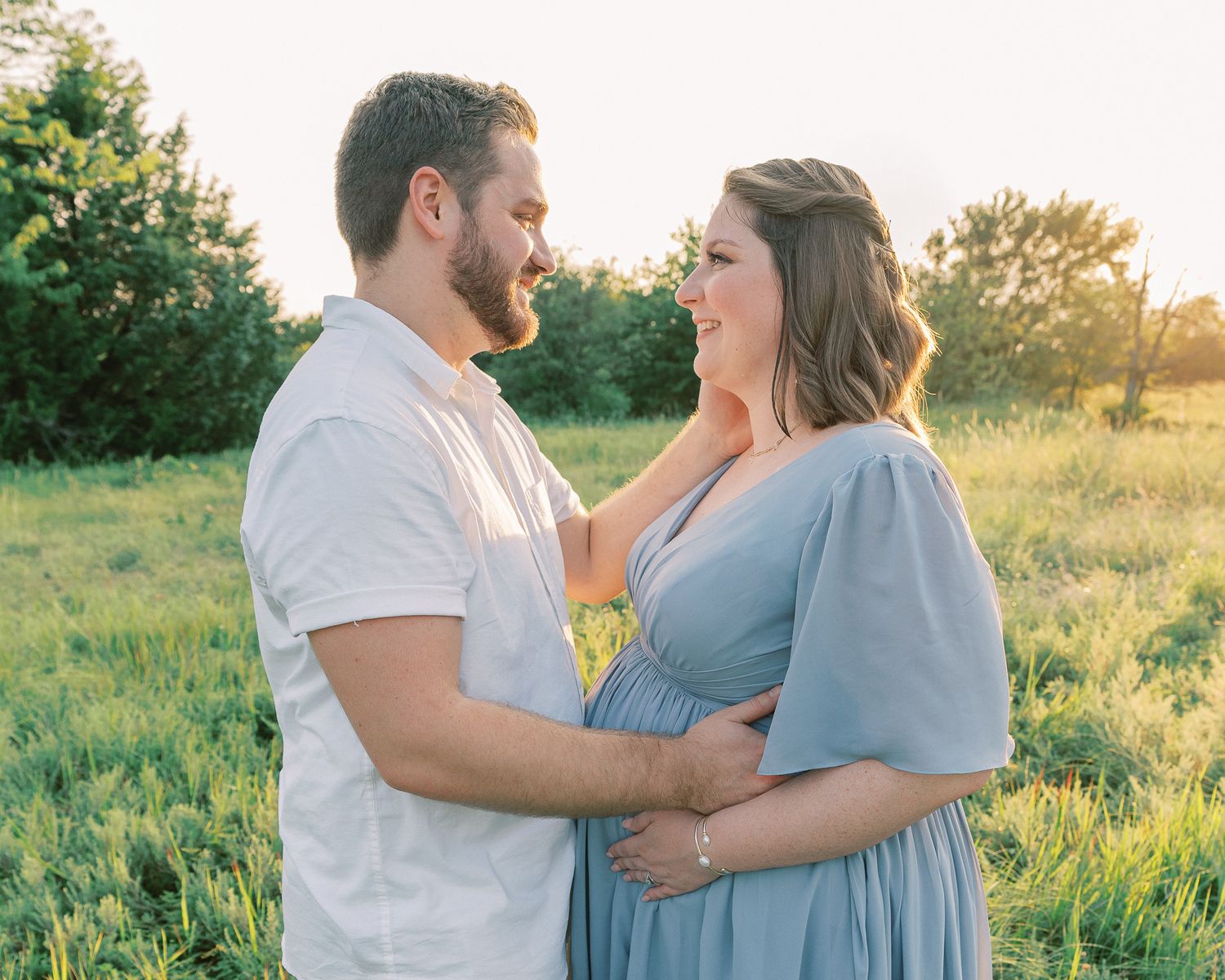 Romantic sunset maternity photo of couple embracing in meadow with golden light.
