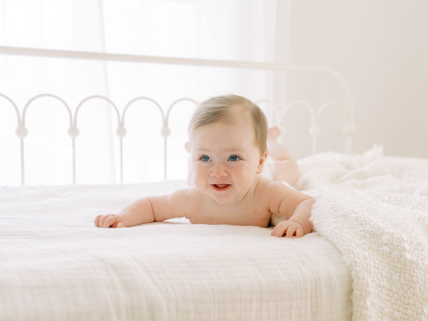 Four serene lifestyle photos of a baby lying on white bedding in a bright, airy room.