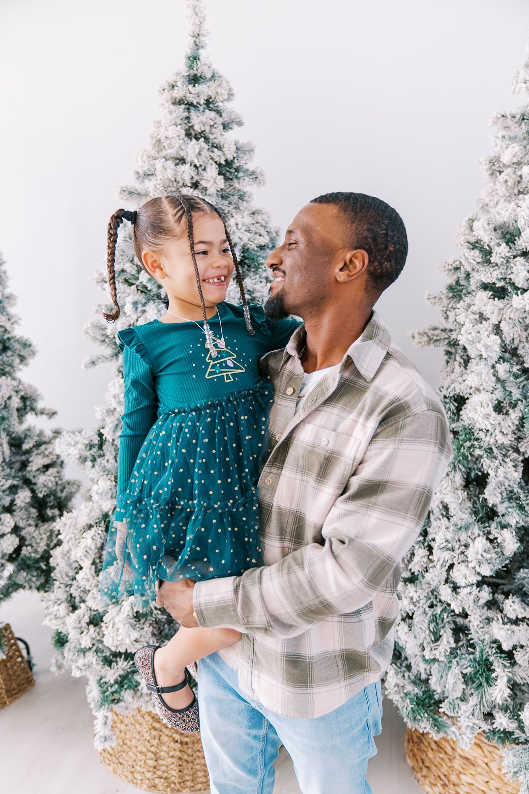 Holiday portraits featuring teal dress and plaid shirt against snow-covered Christmas trees.
