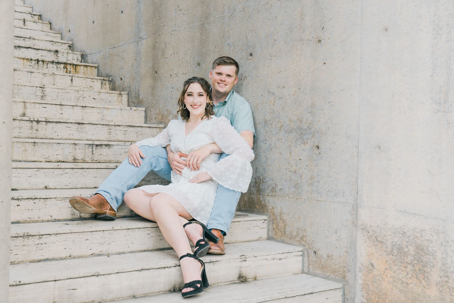 A couple sits together on concrete steps in a romantic engagement photo session.