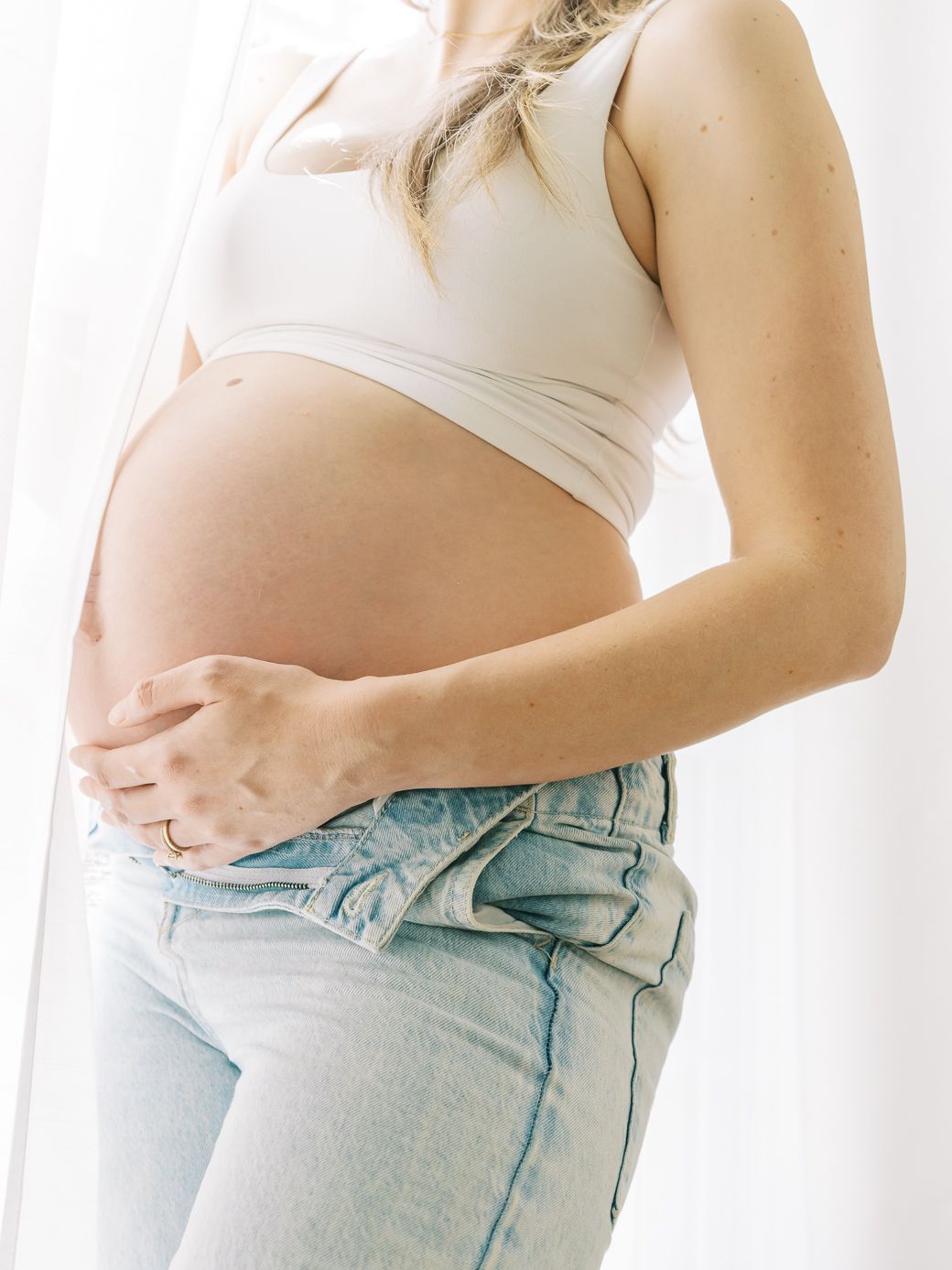 Series of photos showing pregnancy progression in light denim jeans.