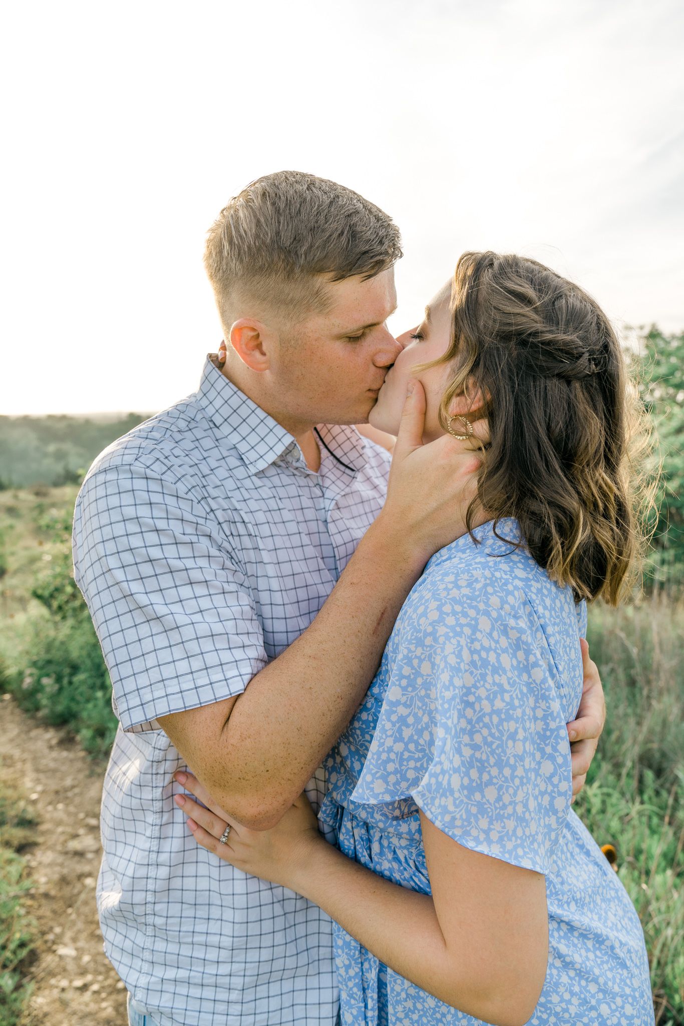 A tender moment between a couple in casual attire sharing kisses in a natural outdoor setting.