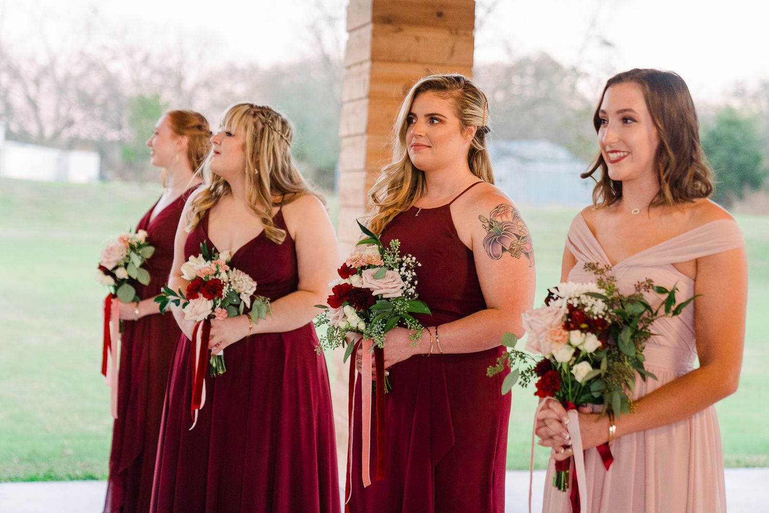 A group in burgundy dresses and floral bouquets share a candid moment during a wedding celebration.