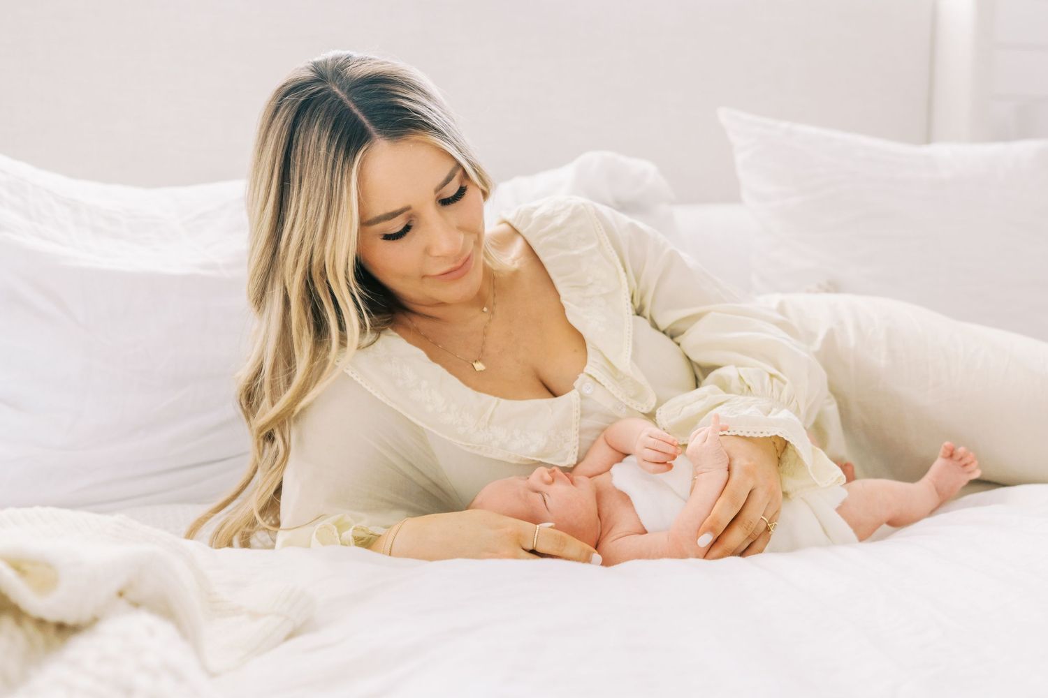 Tender moment between mother and baby on white bedding in soft lighting.