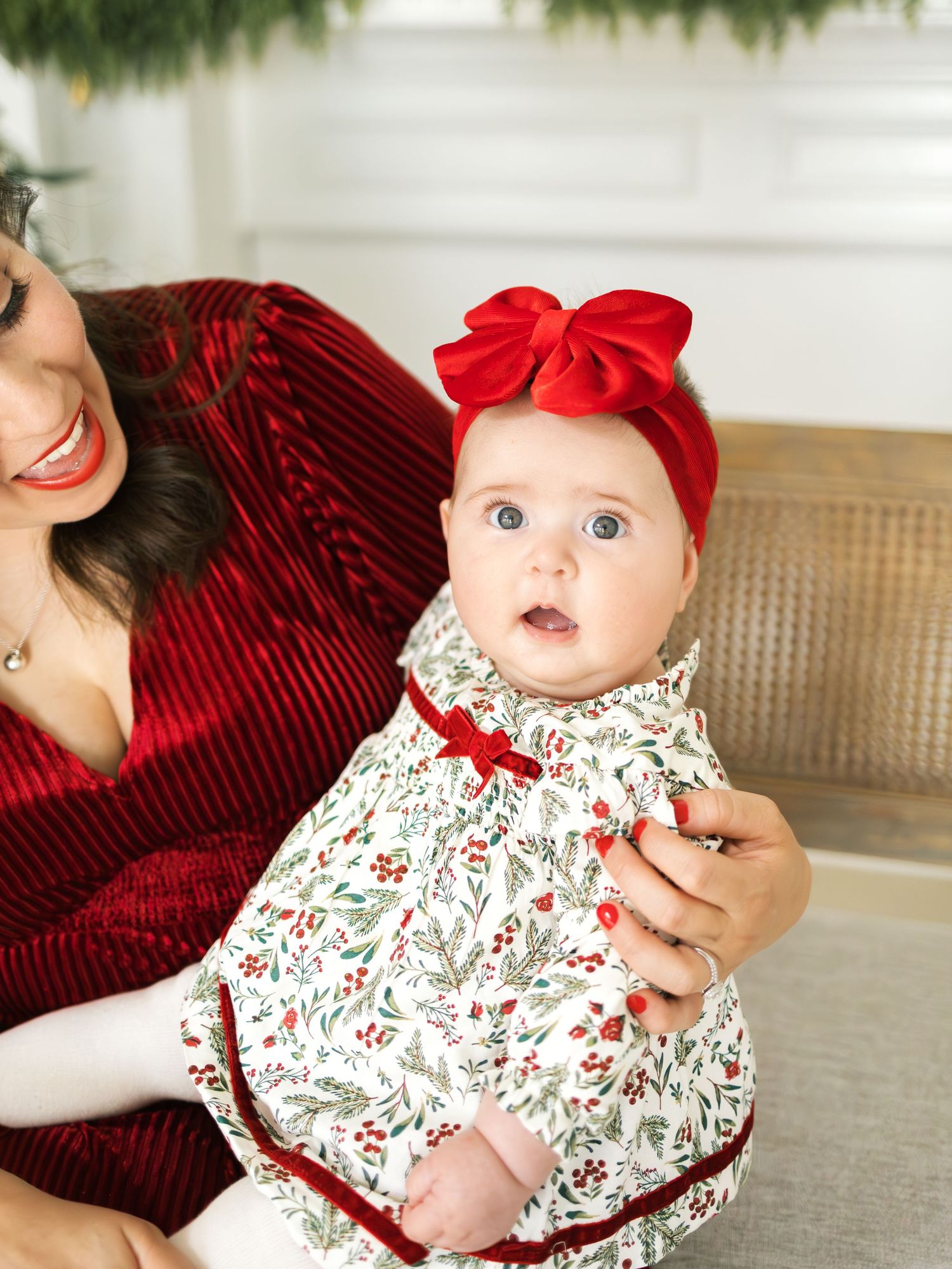 Baby wearing floral dress and red bow sits on wicker chair while being held in series of candid photos.