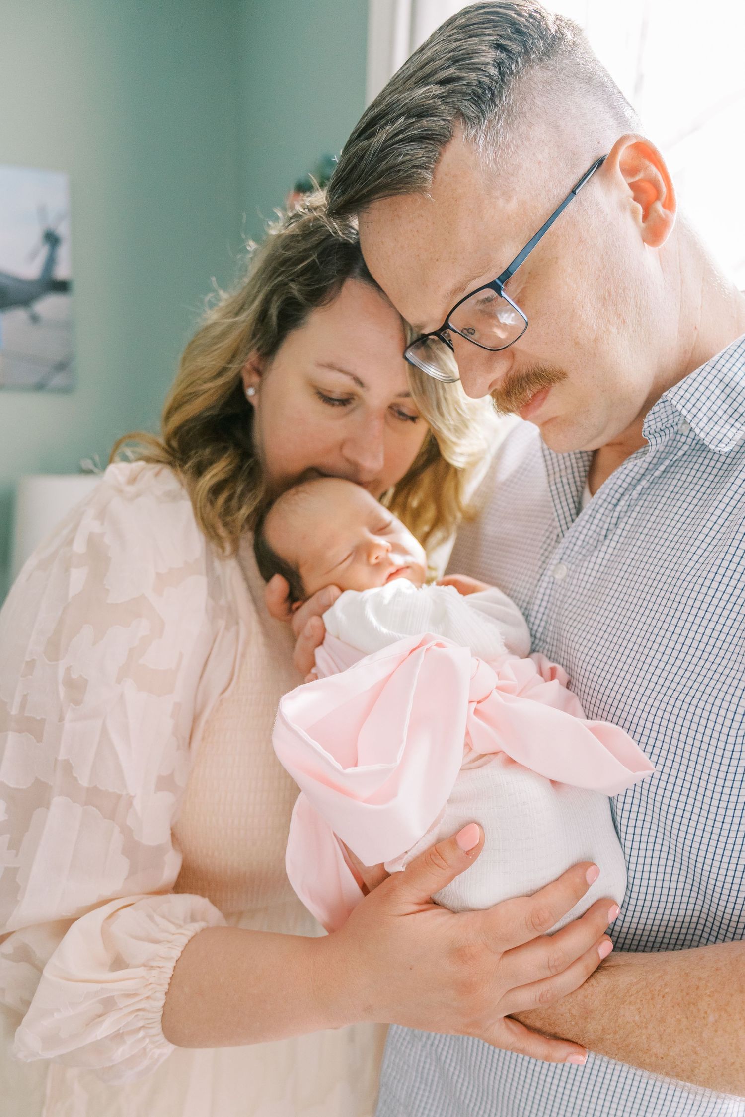 Parents share tender moment with newborn baby wrapped in pink bow blanket.