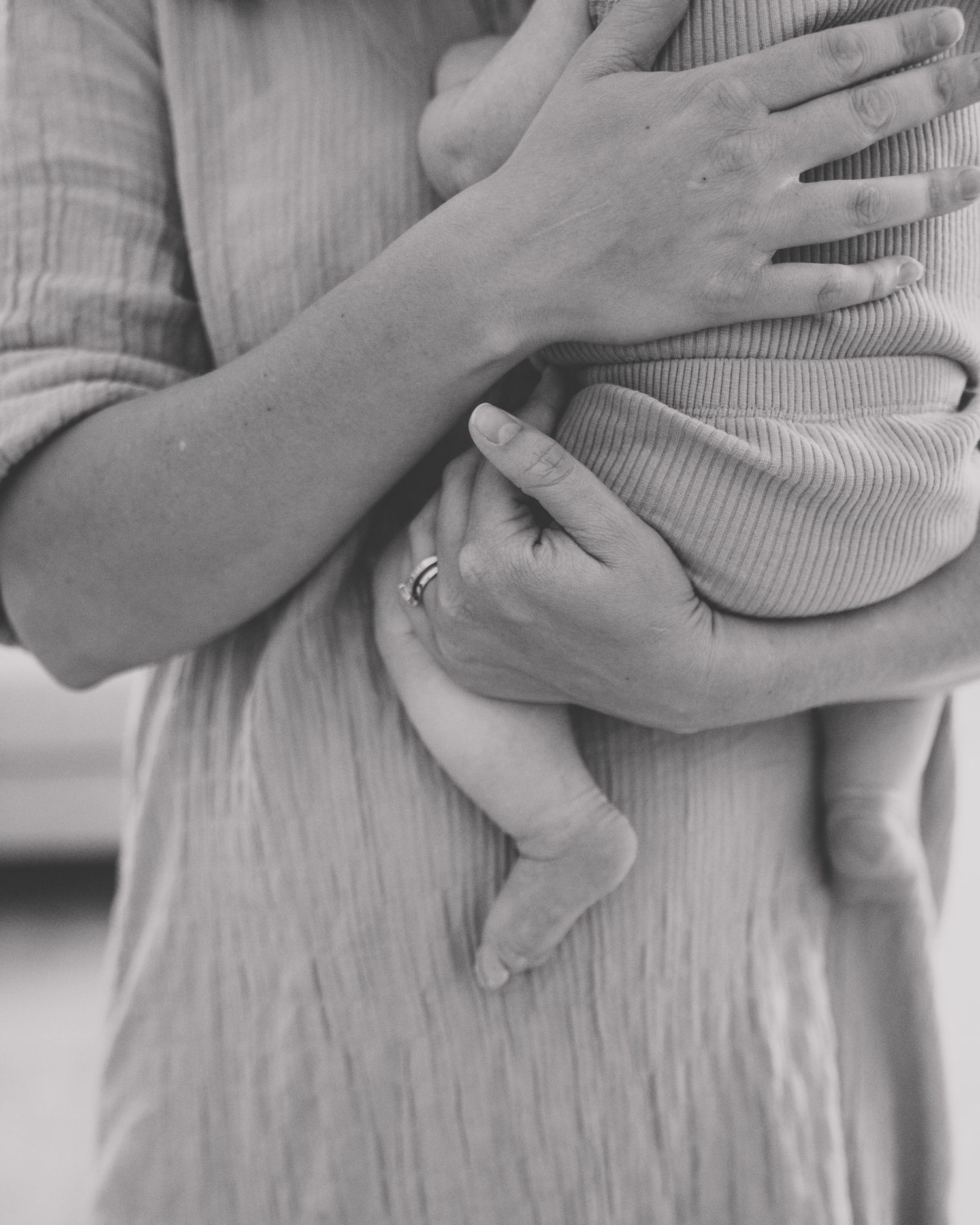 Black and white photo of a mother cradling a newborn baby, wearing a ring, in soft textured clothing.
