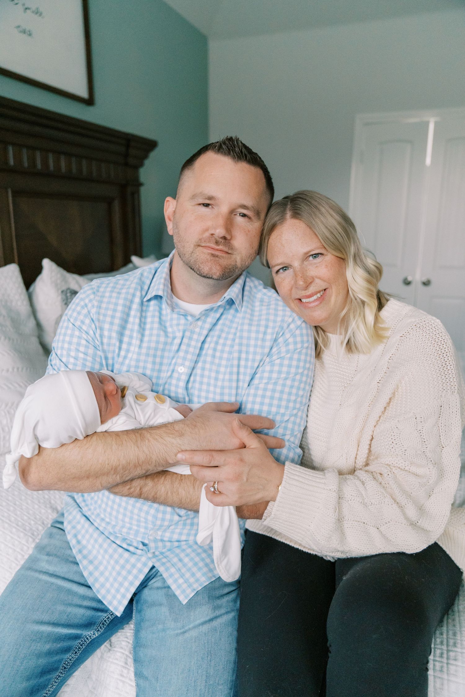 Couple shares tender moment while holding their newborn in cream colored room.