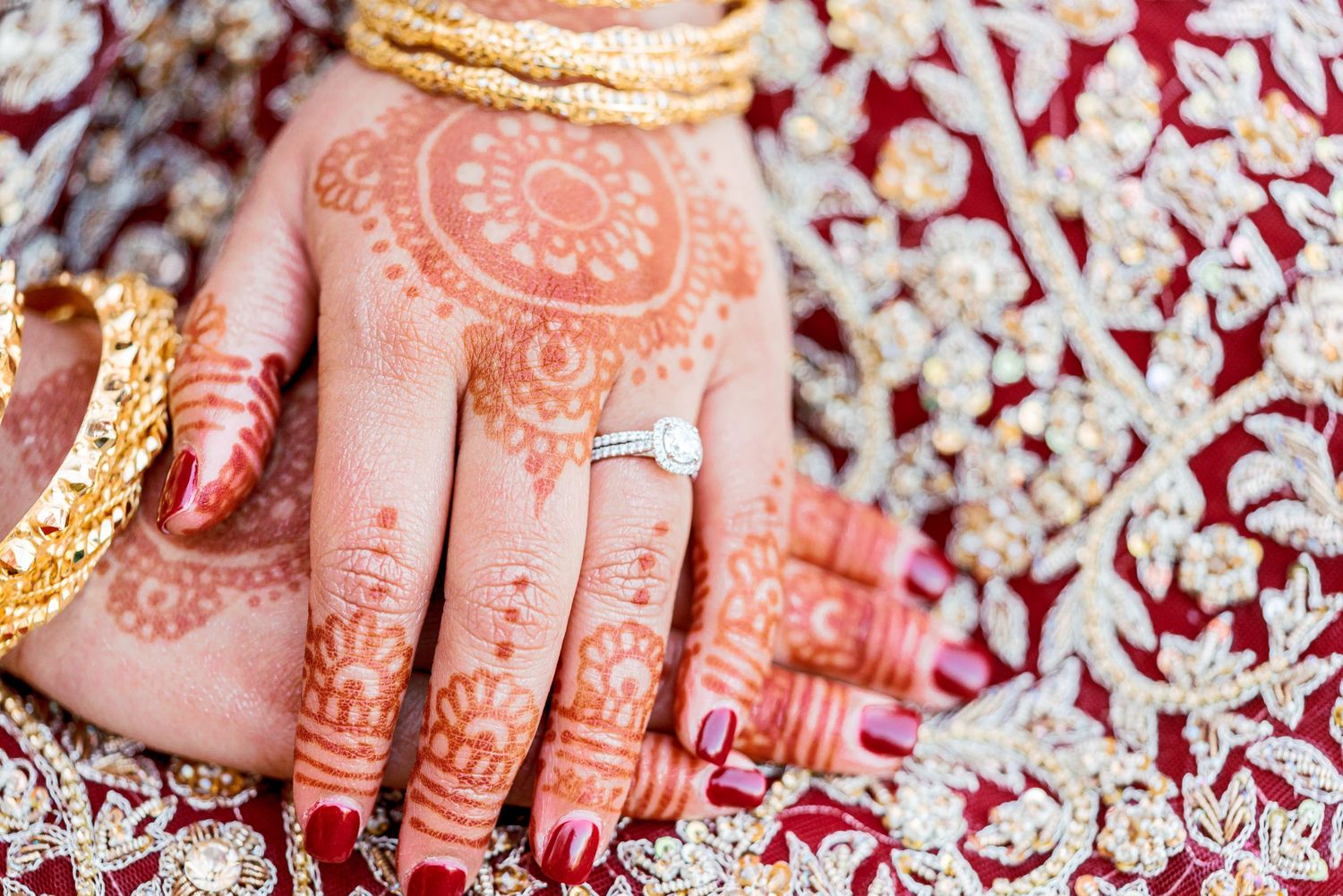 Intricate henna designs adorning hands with traditional Indian bridal jewelry and bangles in rich red and gold colors.