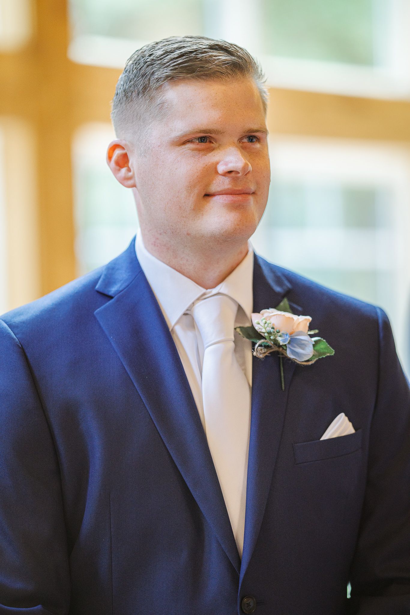 A groom in a navy suit with a white boutonniere smiles softly in a sequence of four similar poses.