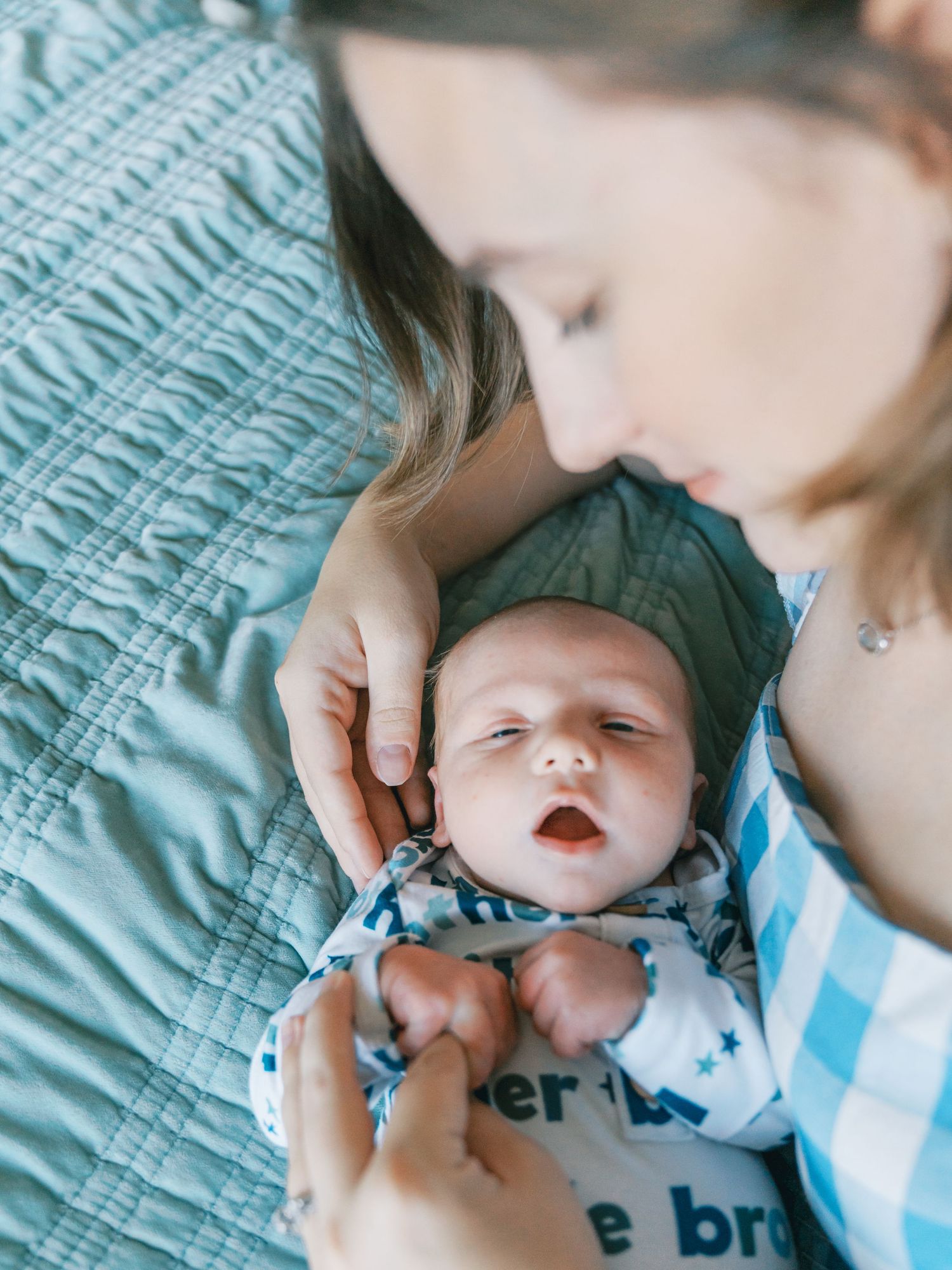 Gentle interaction with a baby wearing blue and white clothing on turquoise bedding.