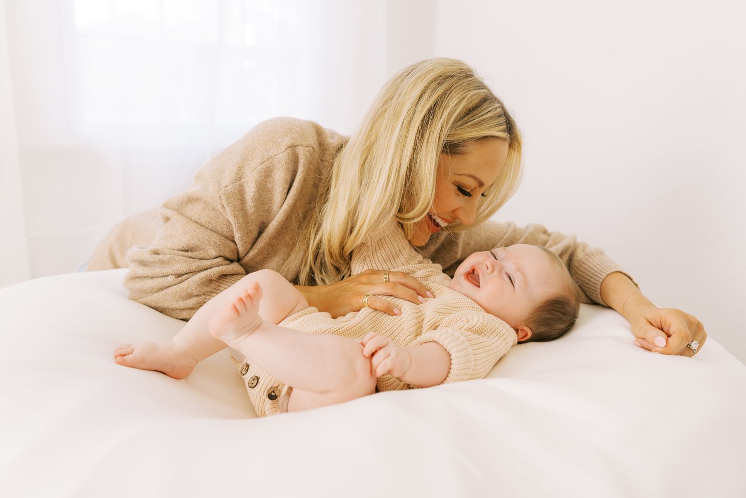 Mother and baby cuddling together on soft white bedding.