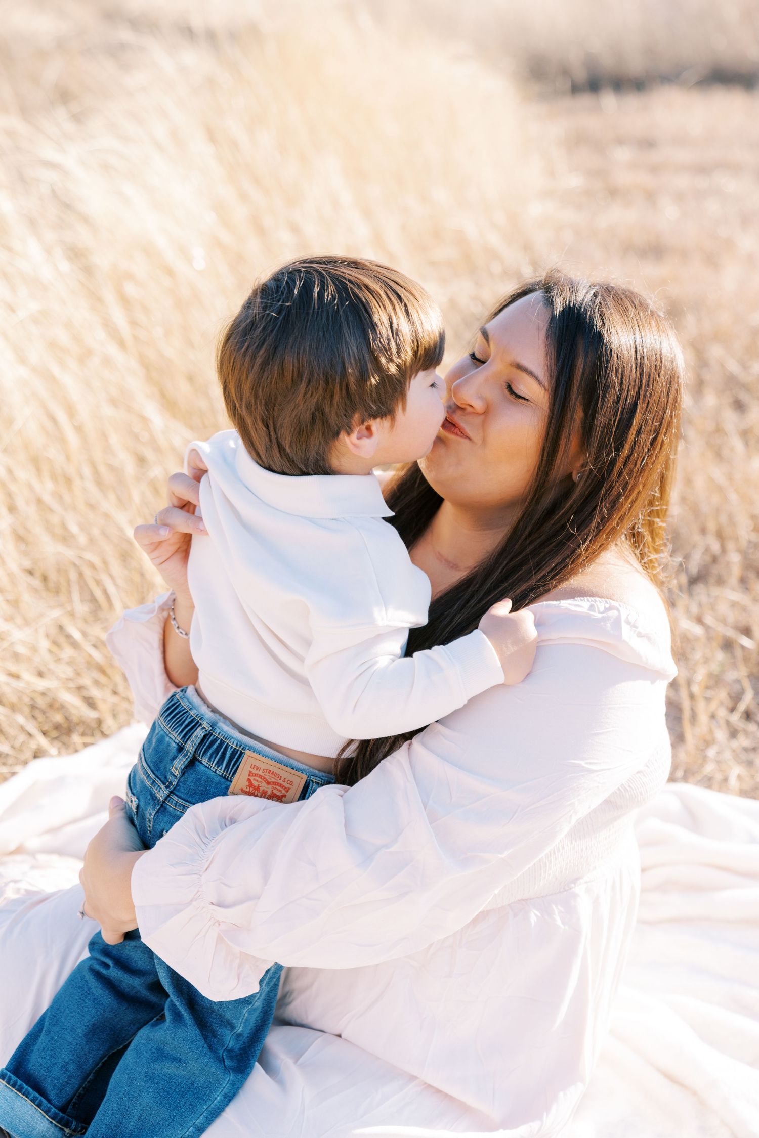 Sweet embrace shared between parent and child on white blanket outdoors.