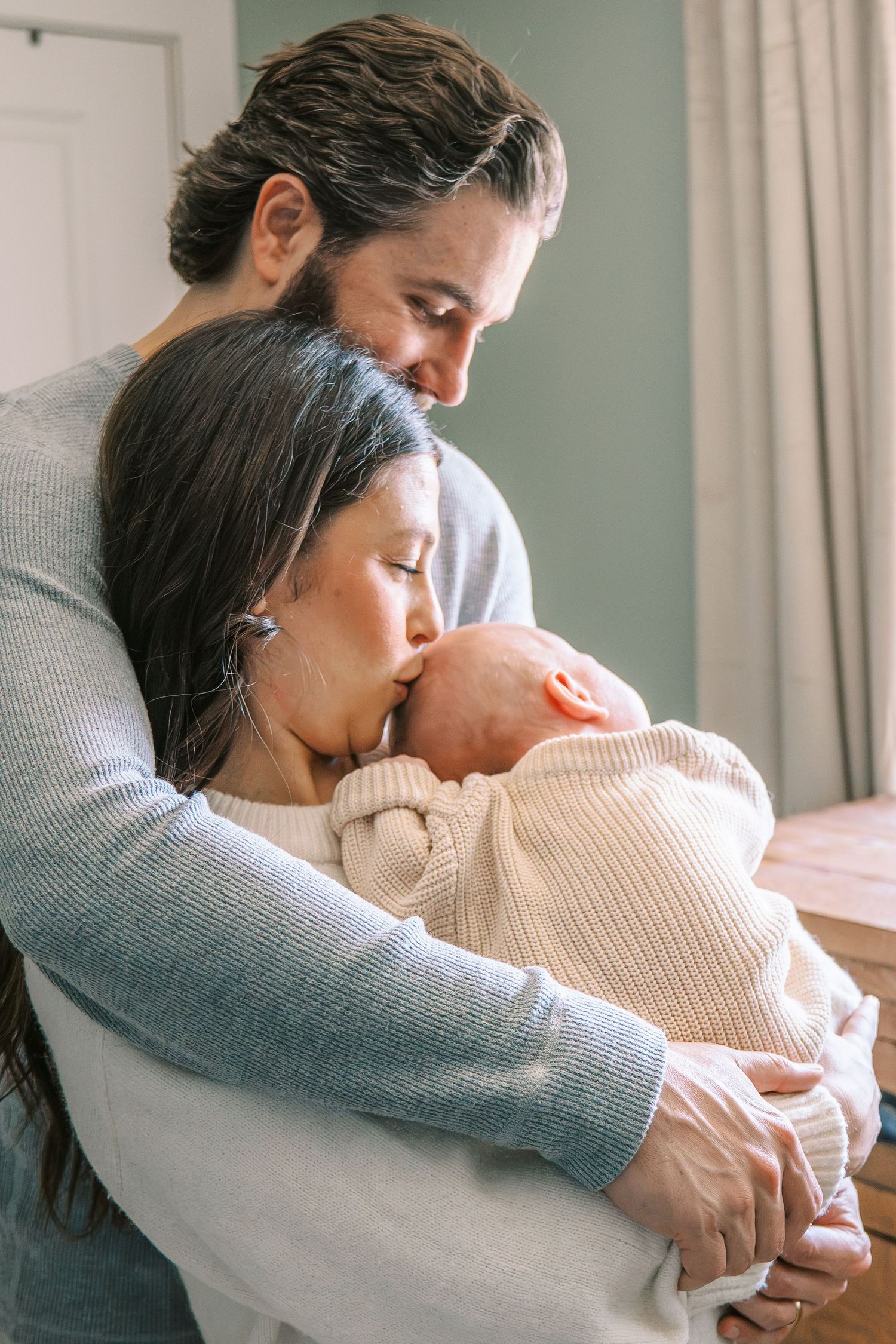 New parents tenderly holding and kissing their newborn baby at home.