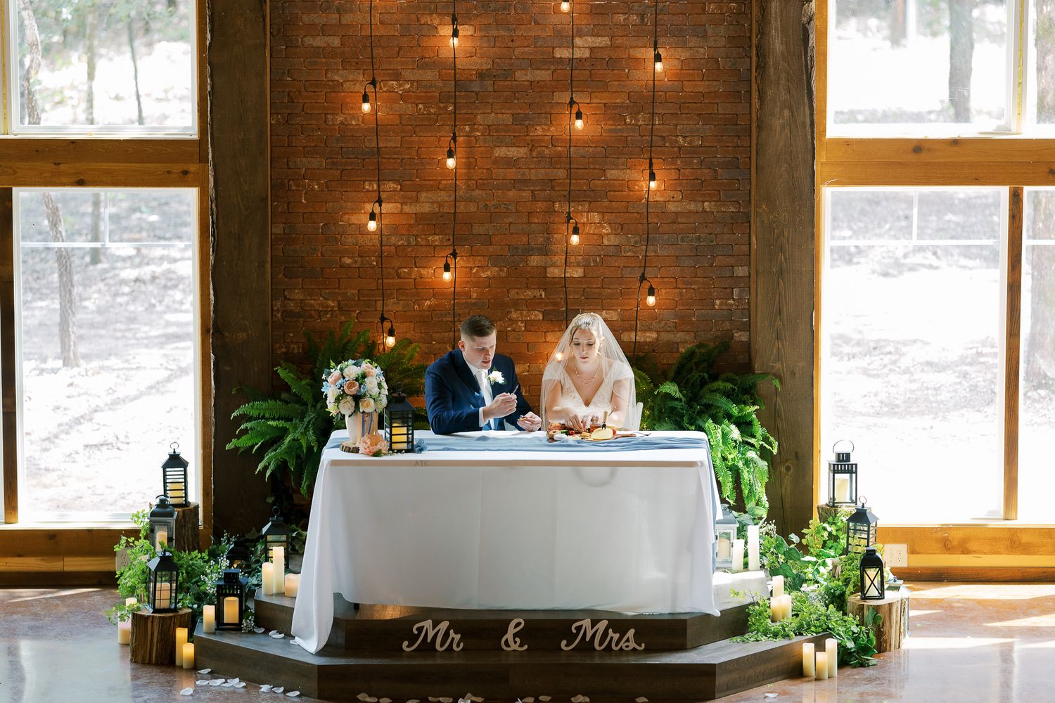 A rustic barn wedding venue with string lights, wooden beams, and large windows letting in natural light.