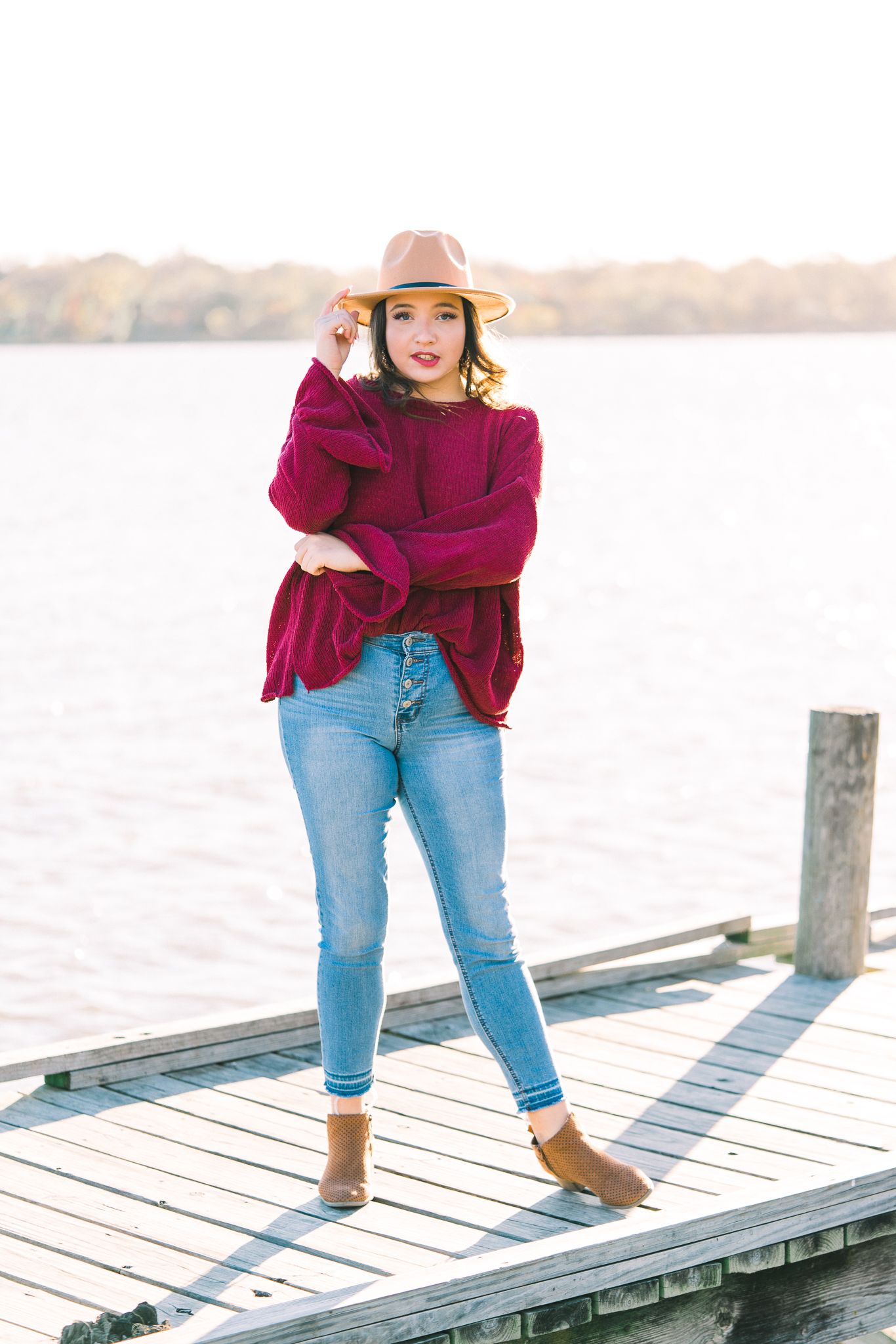 Casual autumn fashion look with burgundy sweater and ankle boots on lakeside wooden pier.