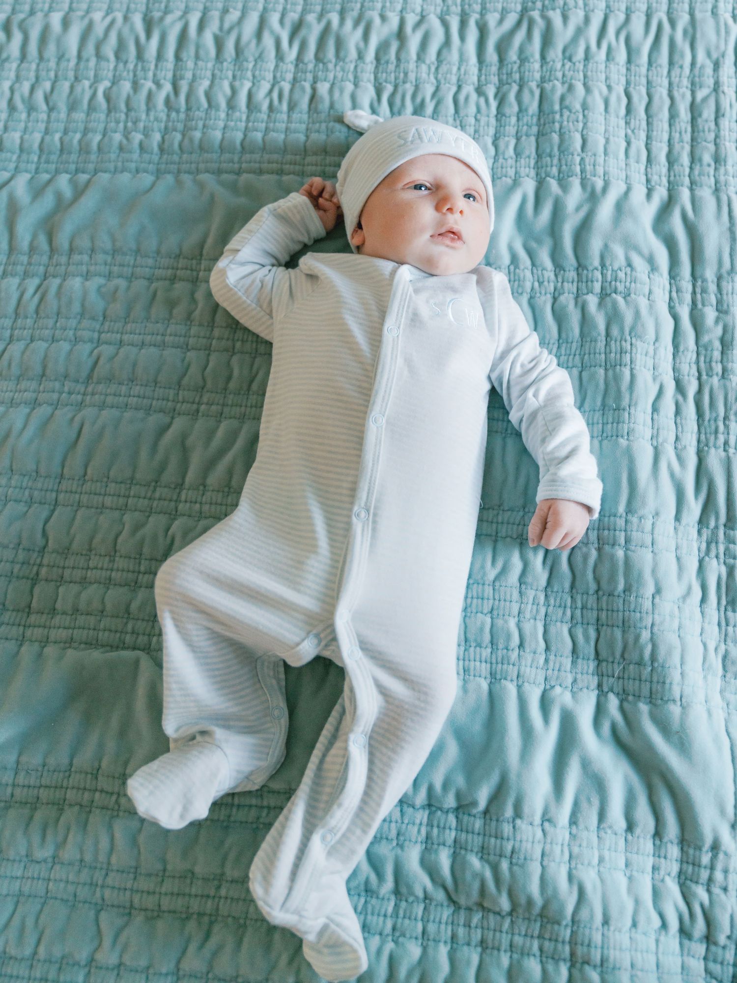 A baby wearing a white onesie lies on a turquoise quilted blanket in a series of connected photos.