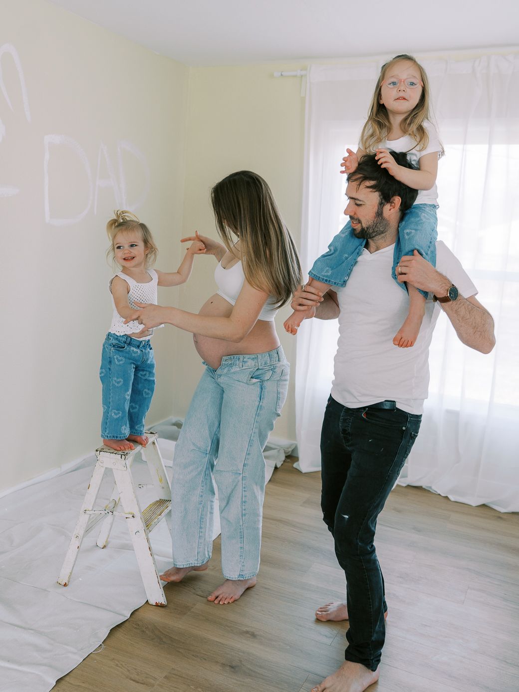 Family dancing and playing together in a bright white room with light wood floors.