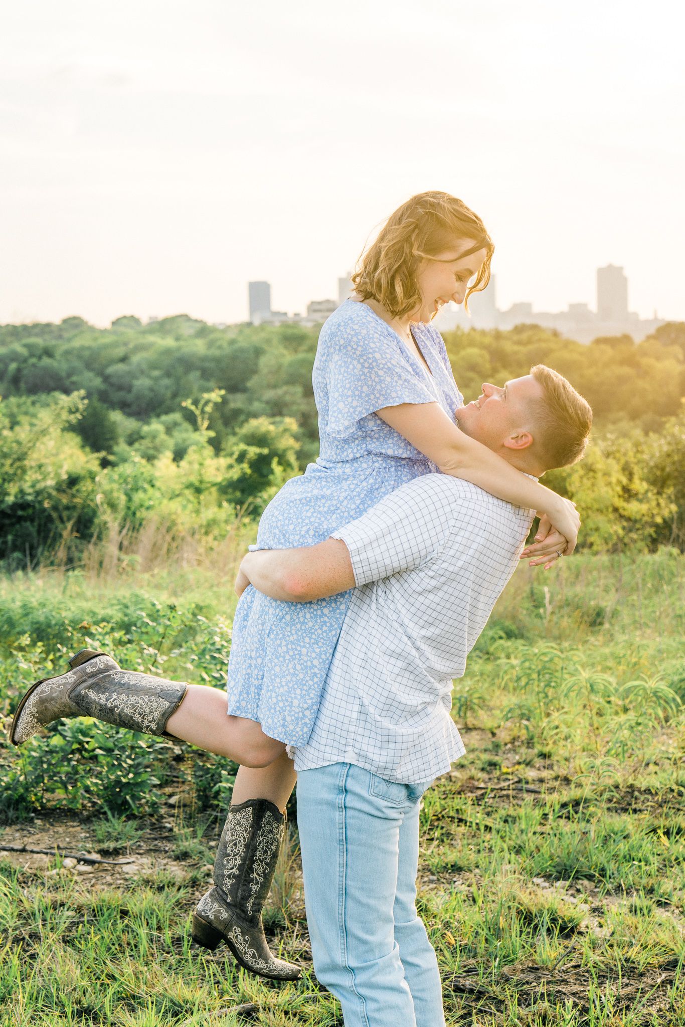 A couple shares a playful moment on a hilltop overlooking a city skyline at golden hour.