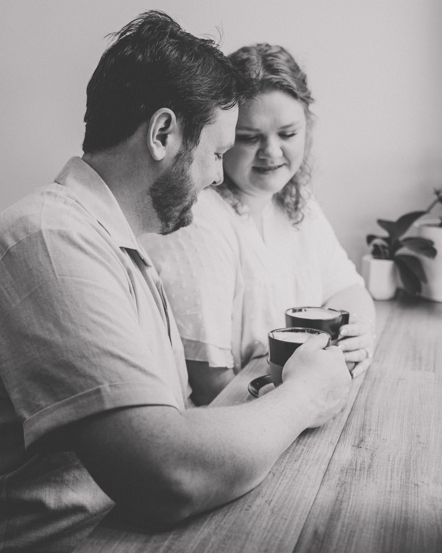 Black and white photo of couple sharing a coffee drink together at a wooden table indoors.