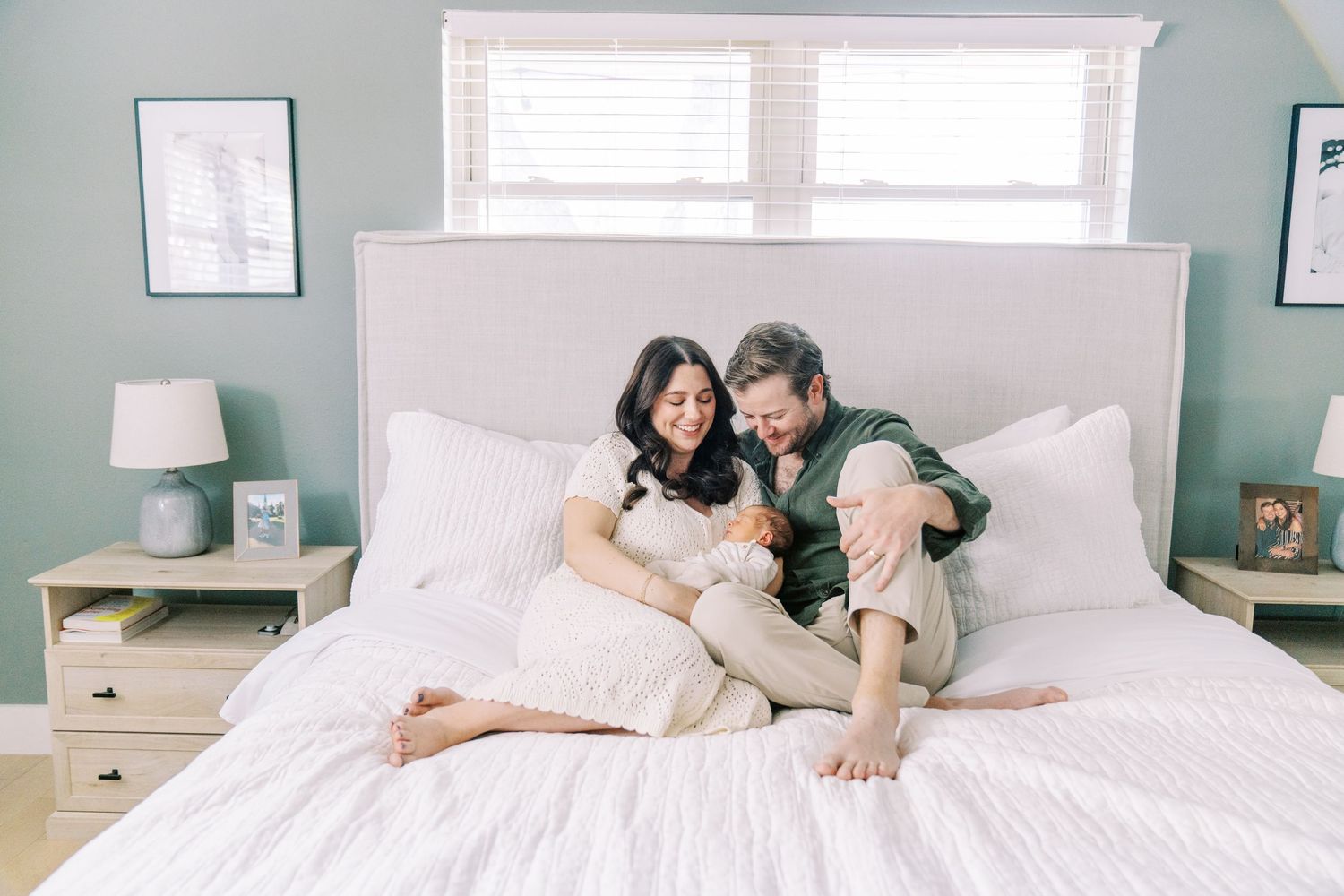 A couple relaxing and playing together on a white bed in a bright, modern bedroom with mint green walls.