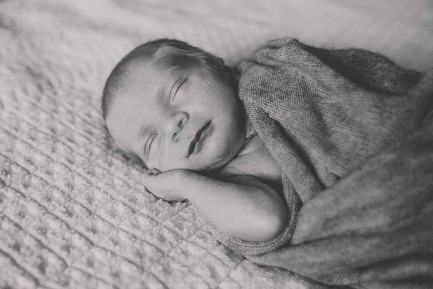 A series of black and white photographs showing a baby sleeping peacefully on textured fabric.