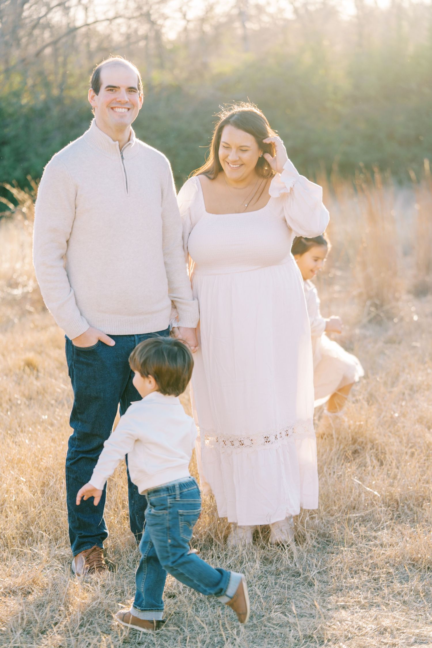 A family wearing coordinated white outfits walks together through a sun-drenched field at sunset.