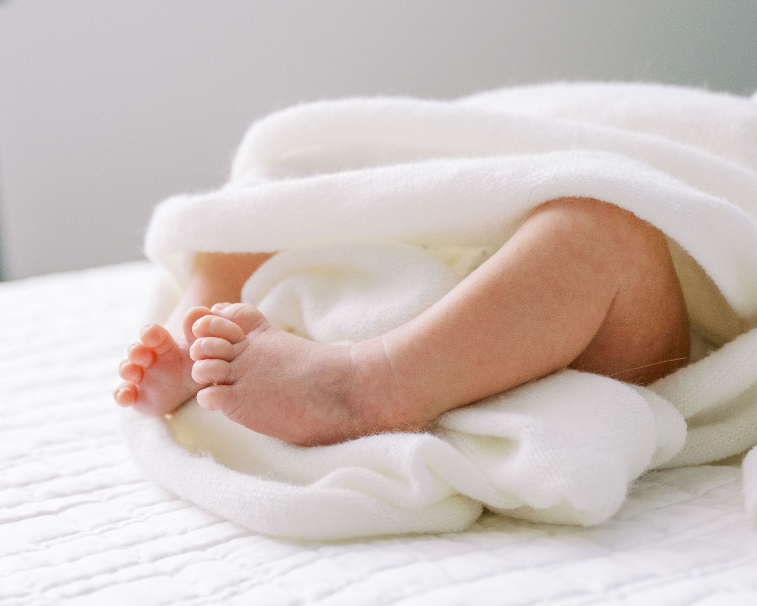 A baby's feet wrapped in soft white blankets on a mattress showing different angles and positions.