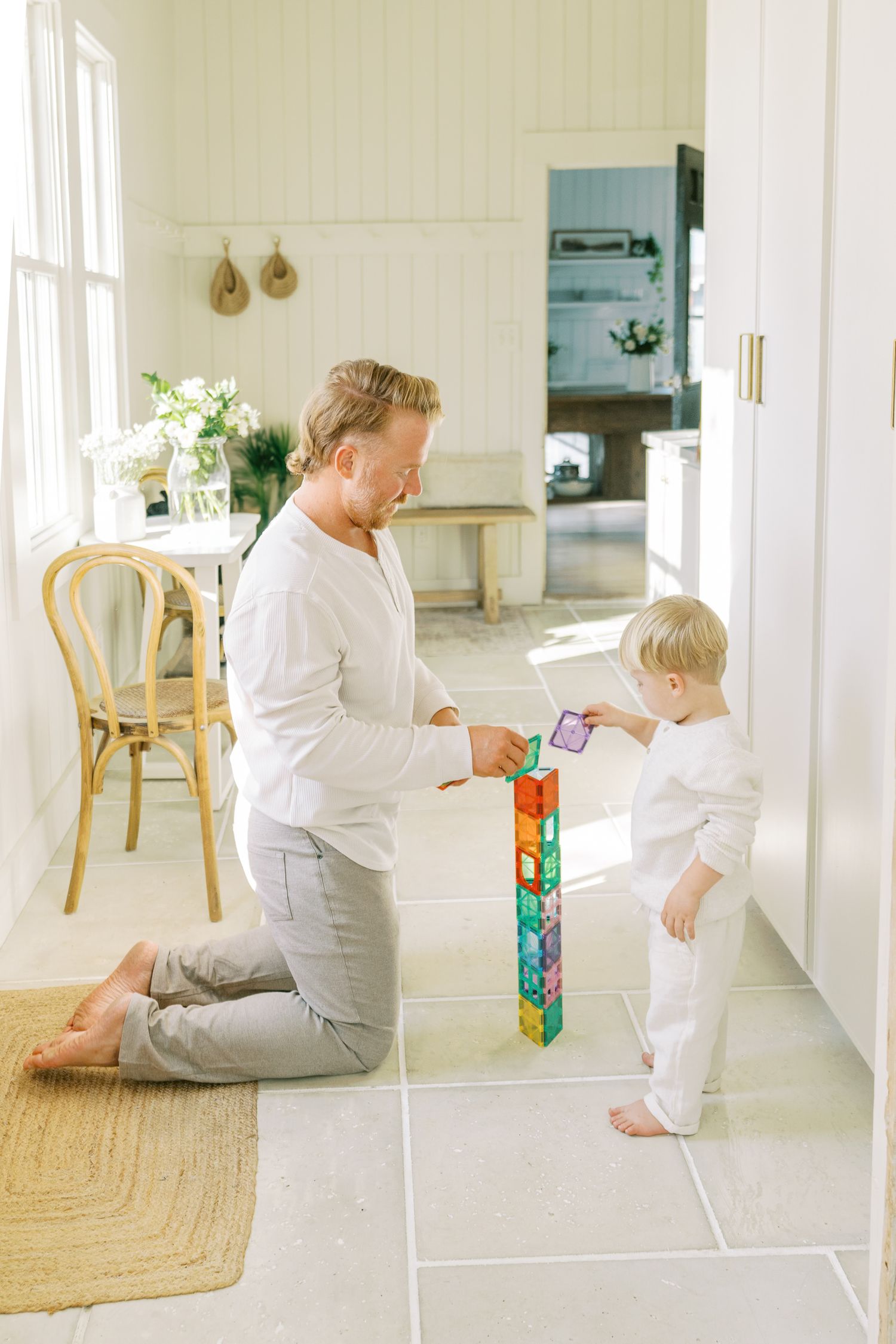 Parent and child playing with colorful blocks on white floor in minimalist interior.