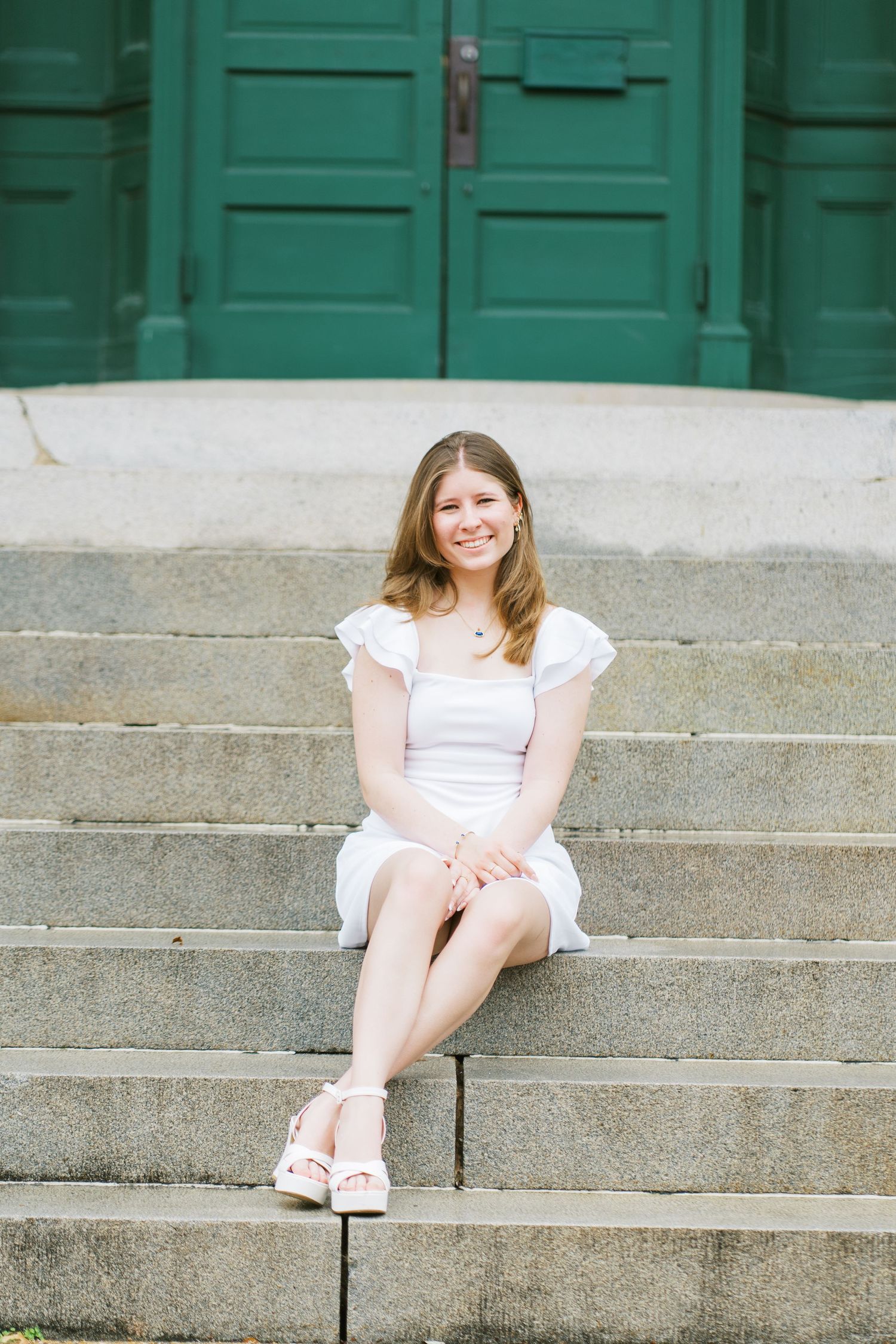 A person in a white dress sits on concrete steps against a teal green wall backdrop.