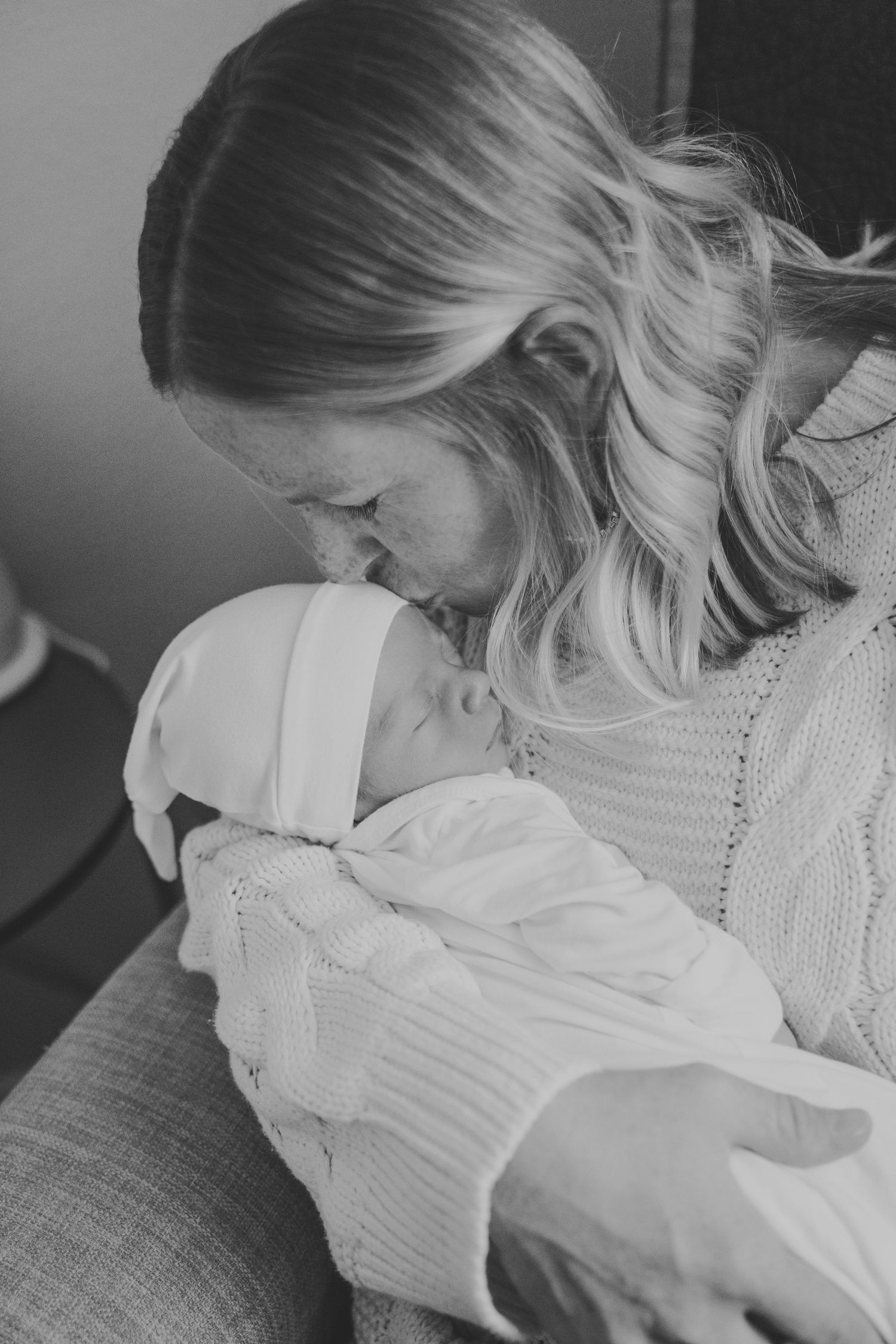 Black and white photo of parent cradling newborn baby in soft knit sweater.