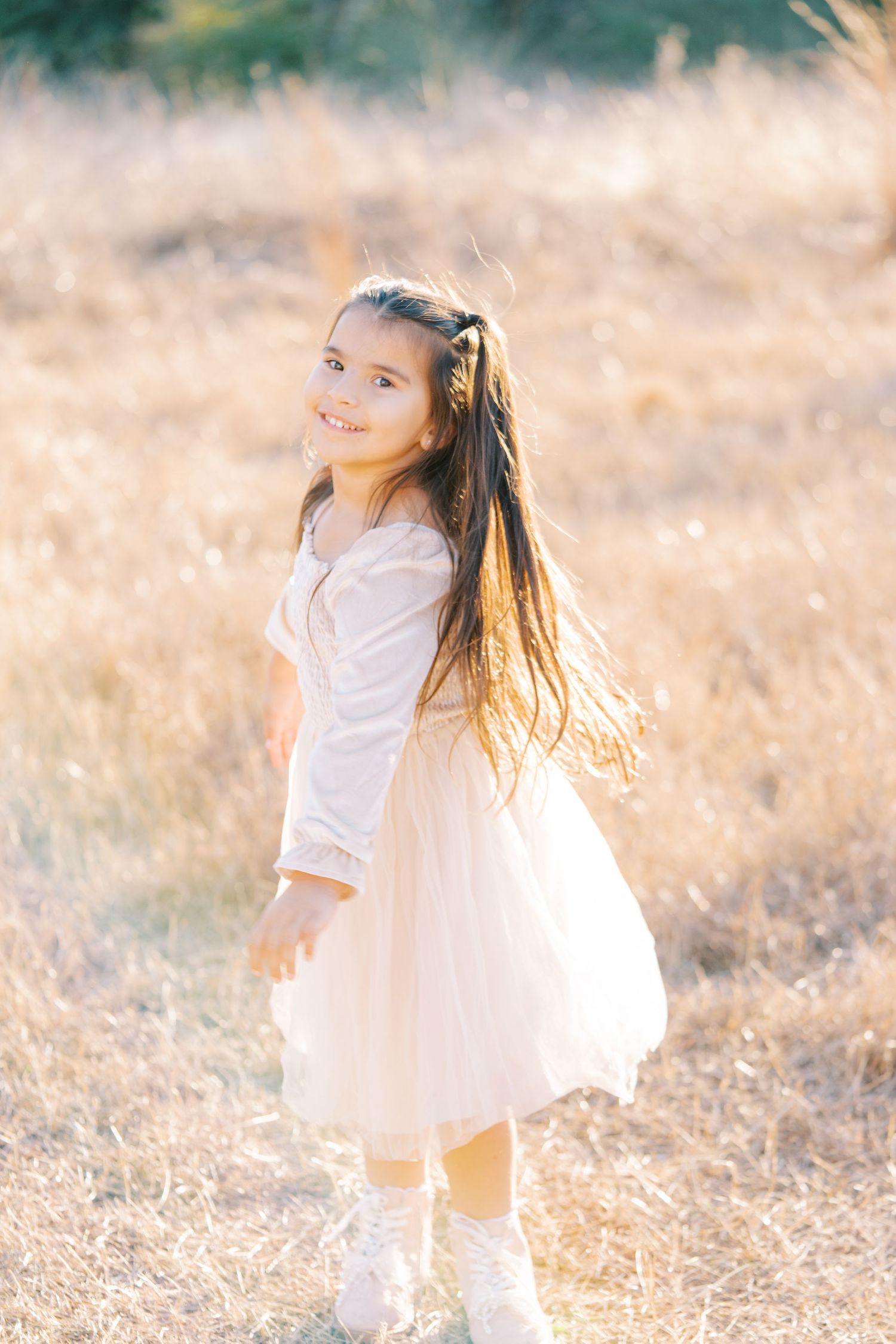 Young child in white dress twirling joyfully in a sun-drenched meadow during golden hour.