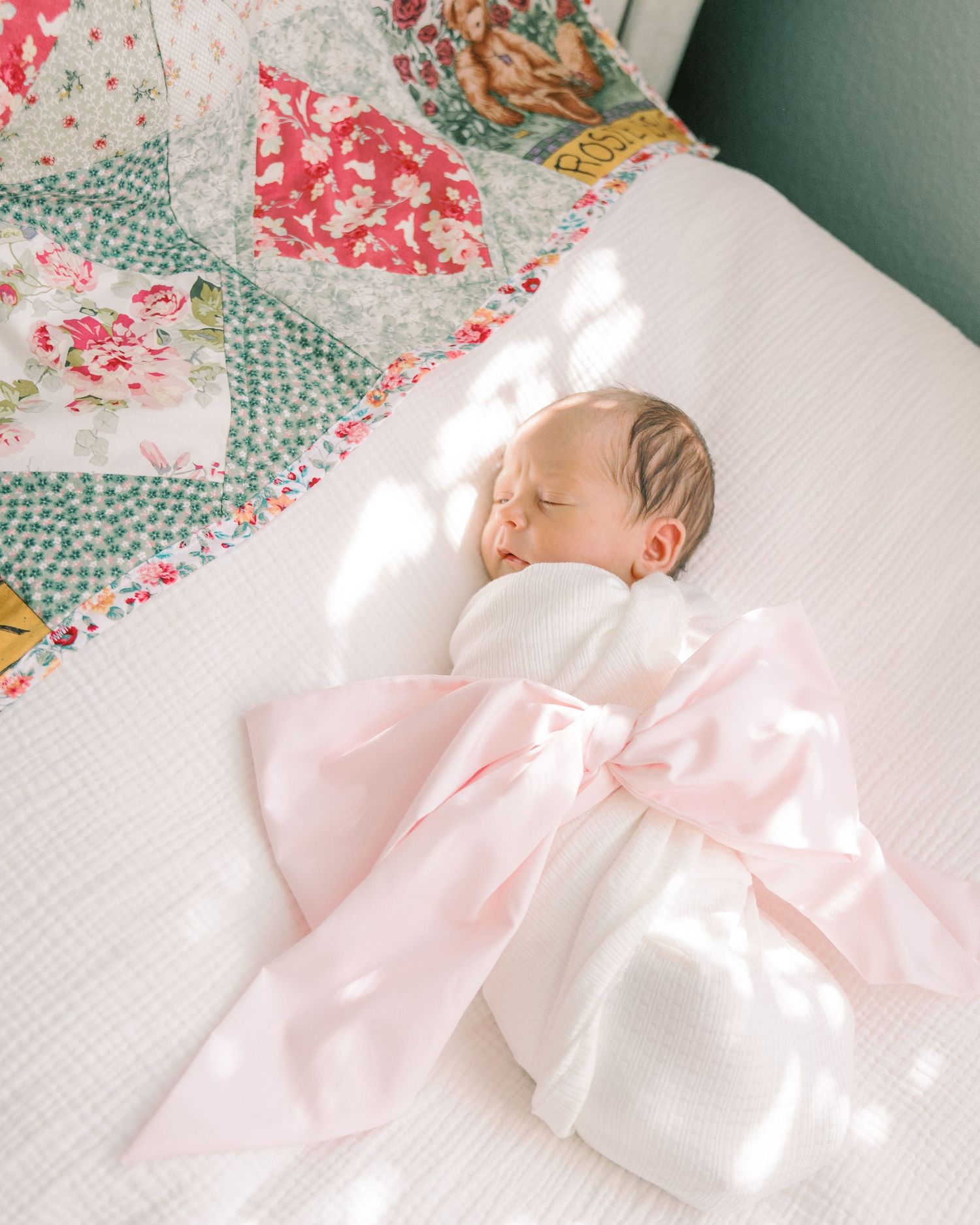 Soft pink and floral patterned bedding creates a delicate nursery scene with natural sunlight streaming in.