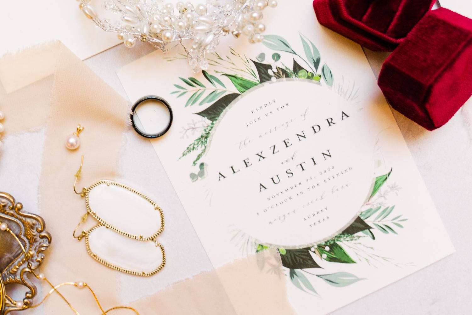 Wedding rings and red velvet ring box displayed with elegant floral invitation cards and delicate gold jewelry.