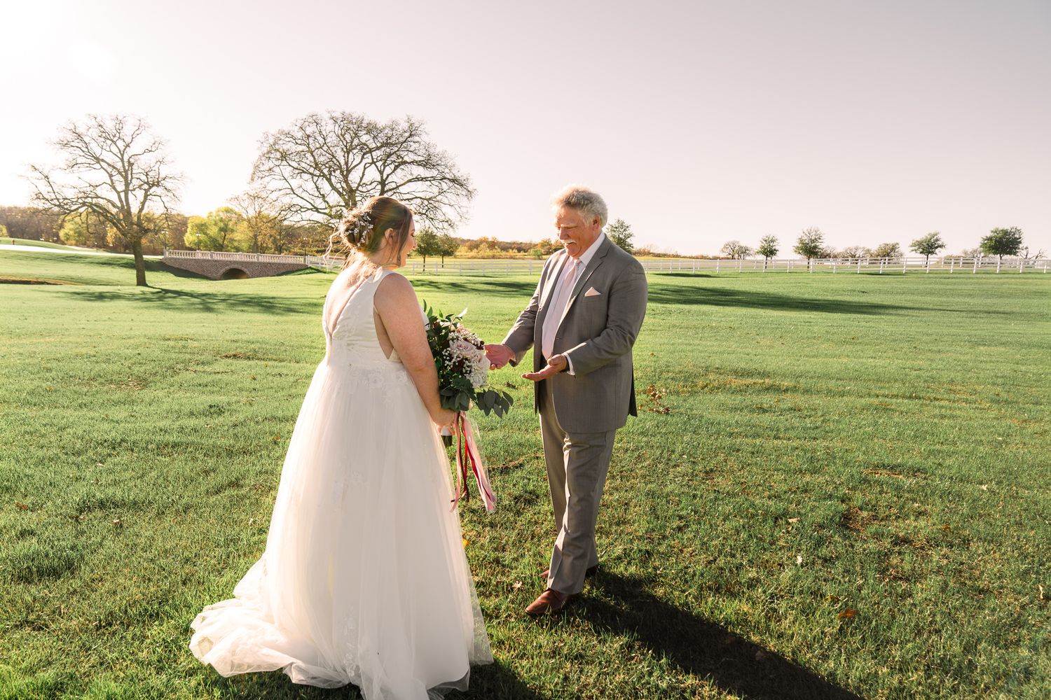 Wedding ceremony taking place in a scenic green field during golden hour.