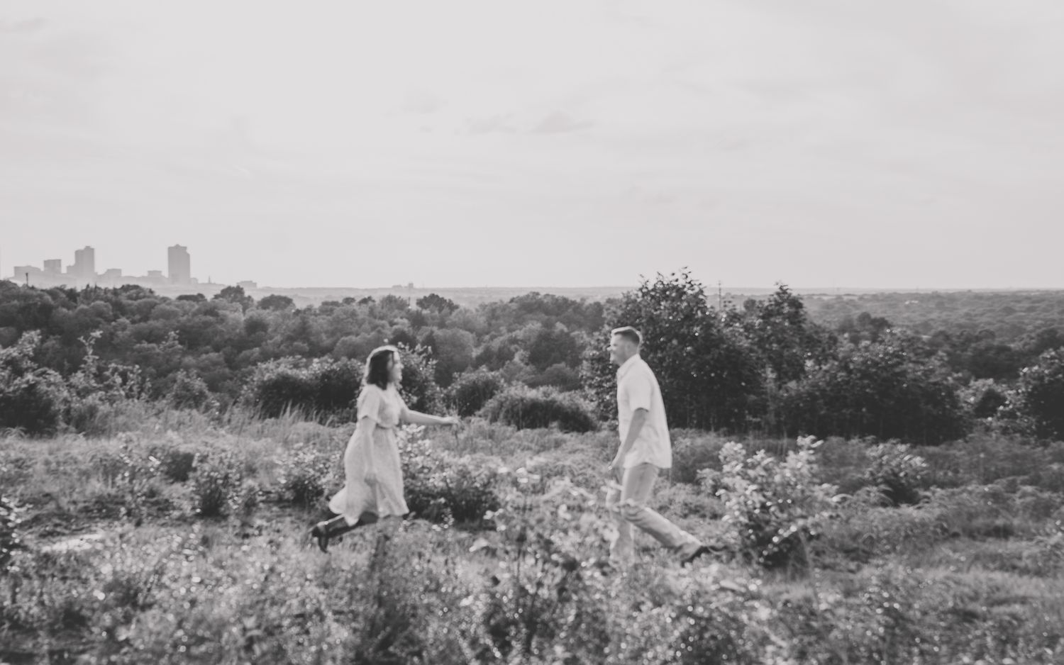 A black and white landscape photo shows people walking through a flowering meadow with a city skyline.