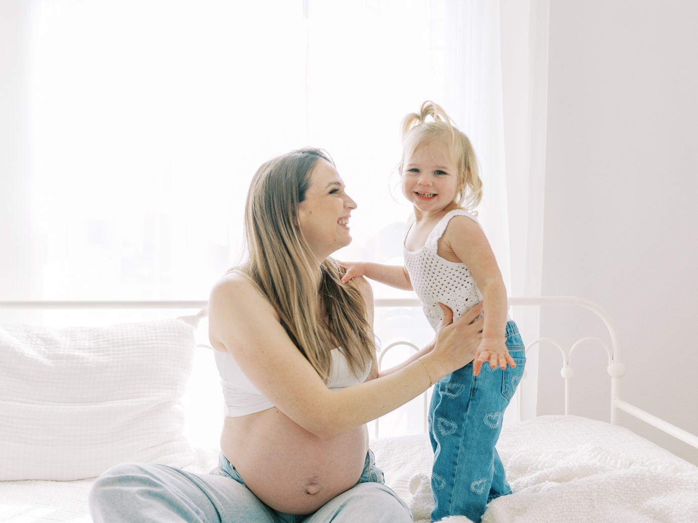 A bright and airy maternity session showing joyful moments between family members on a white bed.