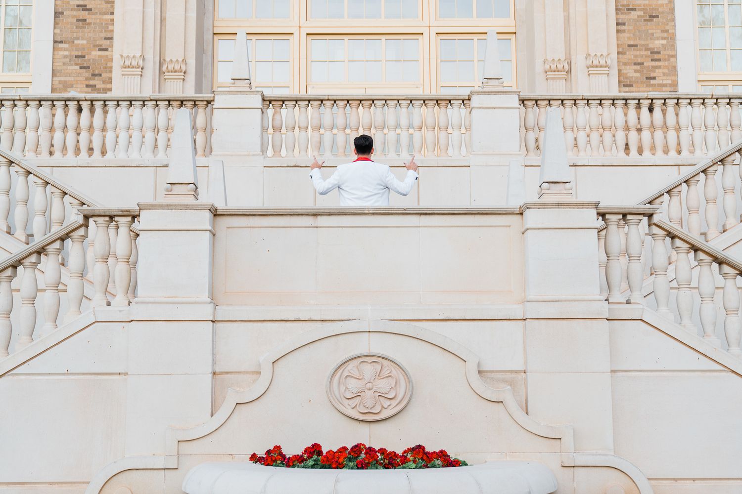 Person in white shirt sitting on grand marble staircase with red flowers at the bottom.