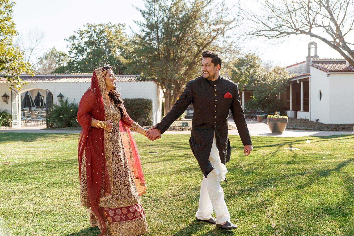 Couple dancing and twirling together on a grassy lawn with white buildings in the background on a sunny day.