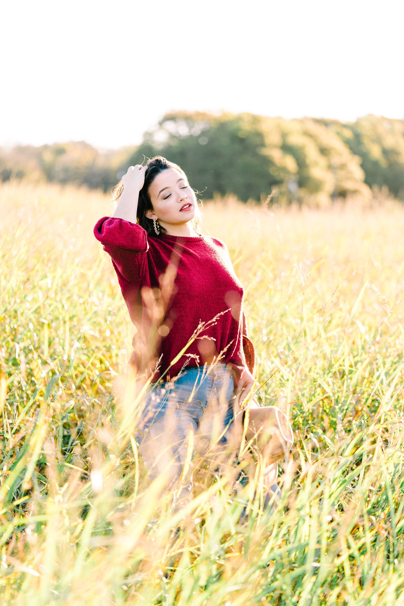 A person in a red top and jeans twirls joyfully in a sunlit golden wheat field during sunset.