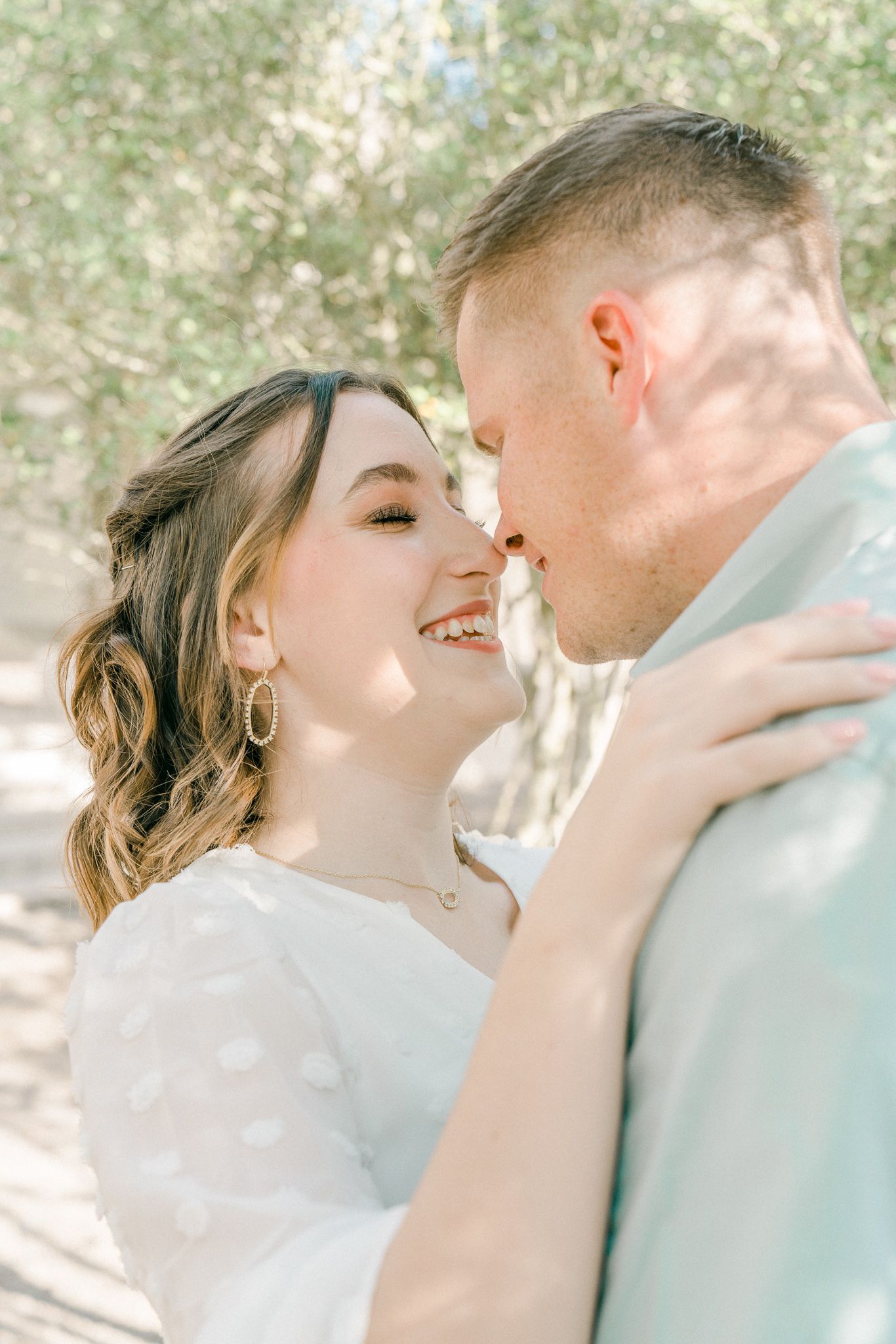 Romantic couple sharing tender kisses in a sunlit outdoor setting with natural lighting and soft focus.