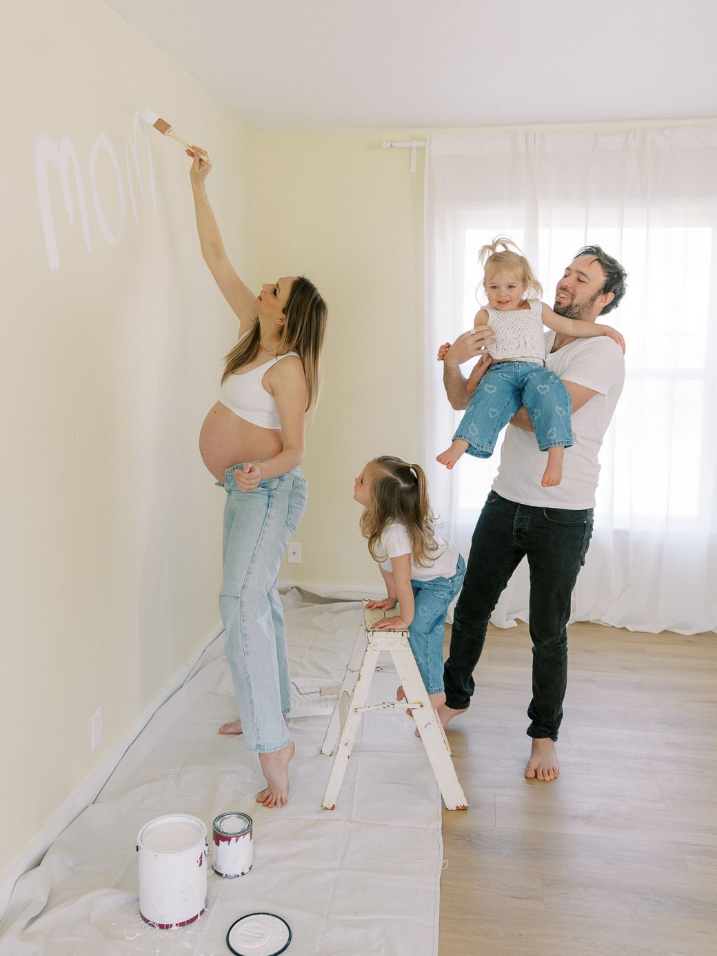 Family plays and dances together in an empty room with white walls and hardwood floors.