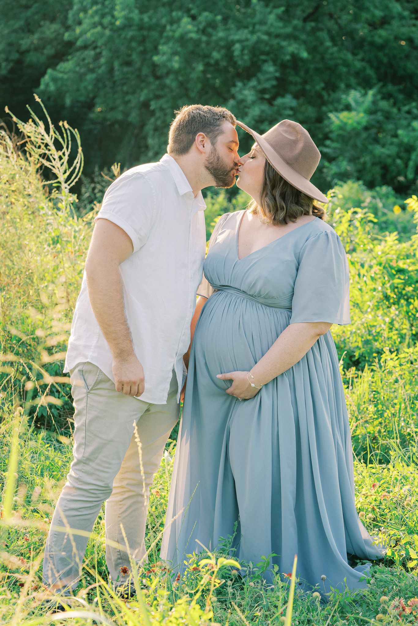 Couple embraces in a lush meadow filled with yellow wildflowers and green foliage on a sunny summer day.