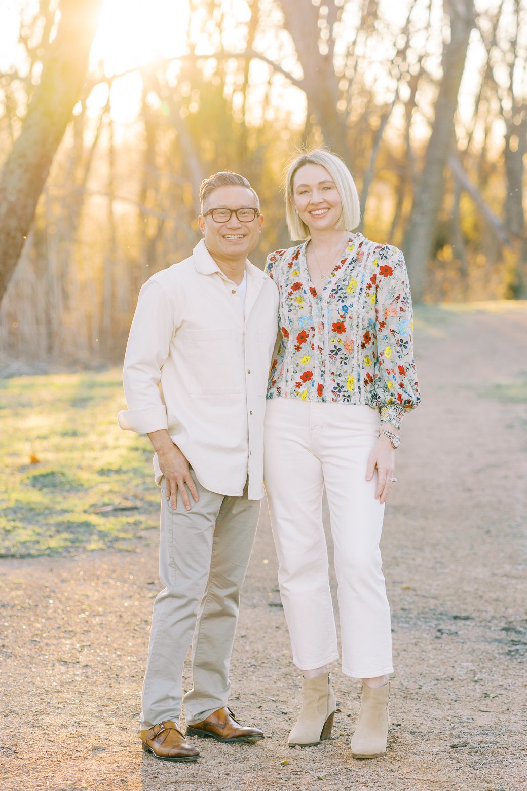 A couple walks together on a dirt path during golden hour sunset in a wooded area.
