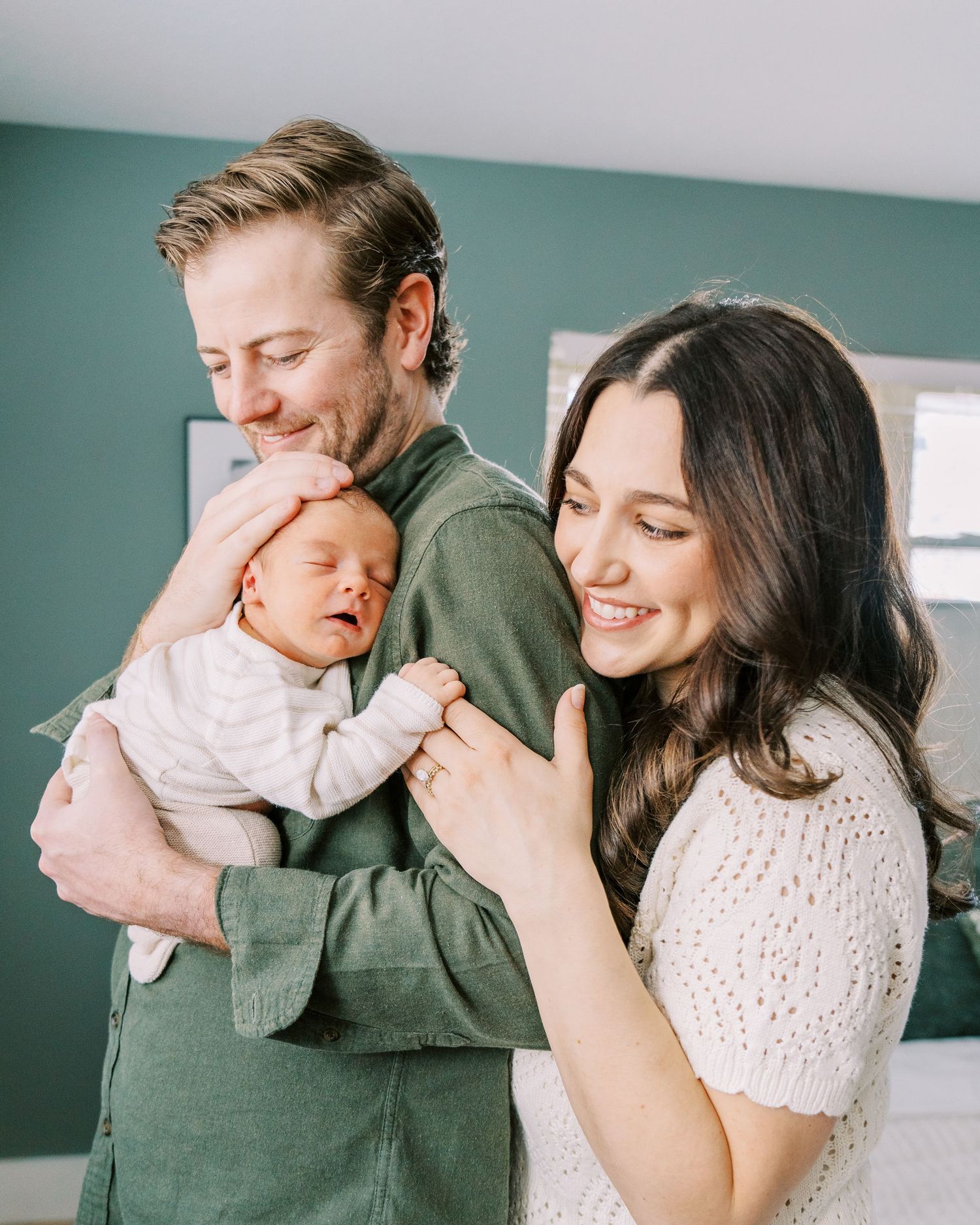 A family shares tender moments together in a bright room with teal walls, wearing cozy sweaters.