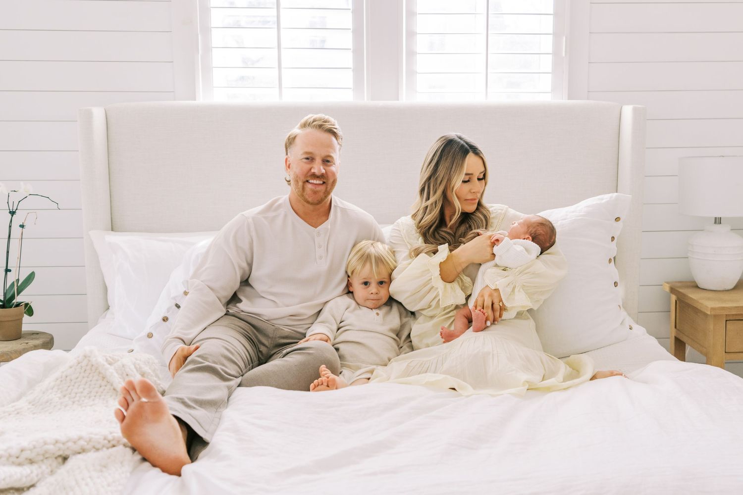Family shares tender moments together on a white bed in a bright sunlit room.
